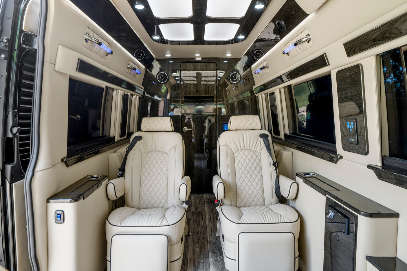 Elegant RV rental interior featuring two cream captain's chairs, dark wood trim, ambient lighting, and comfortable amenities.