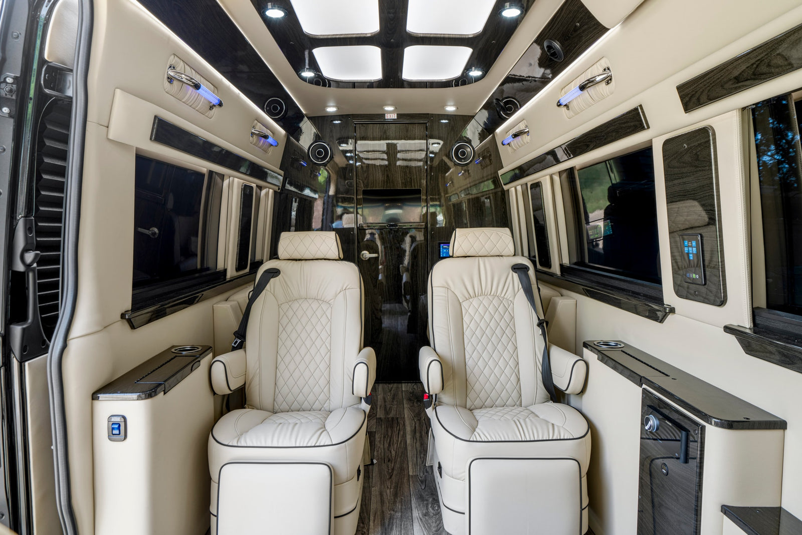 Elegant RV rental interior featuring two cream captain's chairs, dark wood trim, ambient lighting, and comfortable amenities.