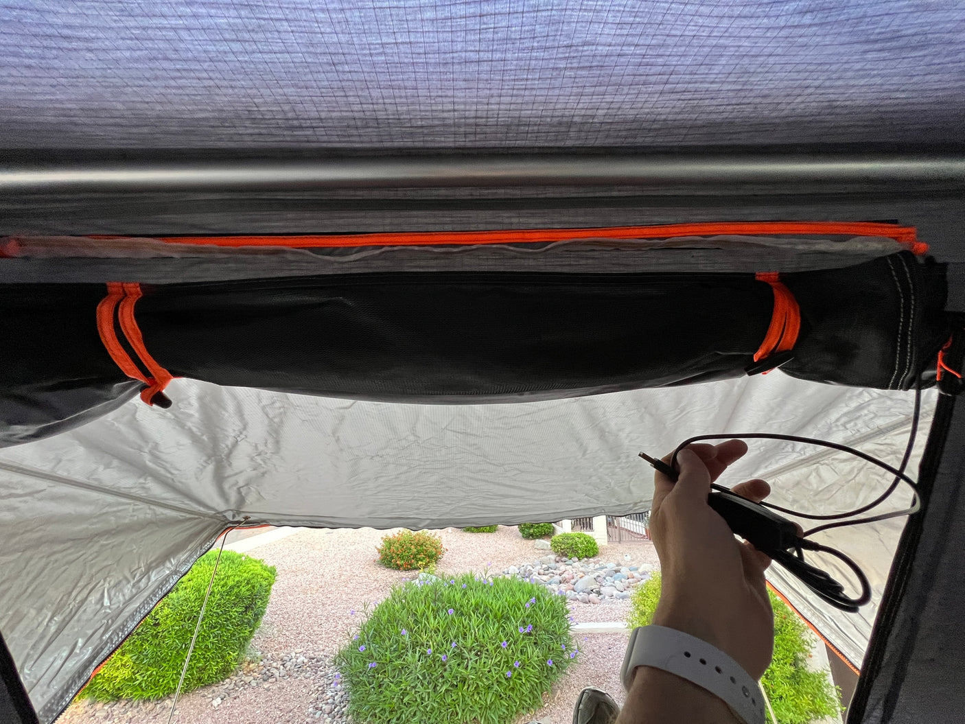 Inside an RV rental tent, a hand holds a power cable, showing the structured interior and outdoor yard view.