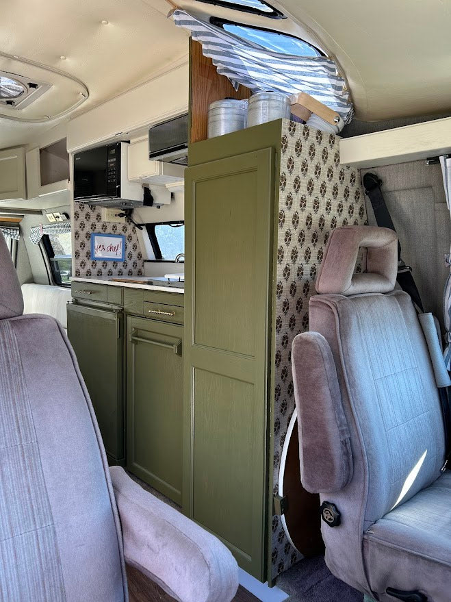 This RV rental interior showcases a charming kitchenette with green cabinets, patterned accents, and comfy front seats.