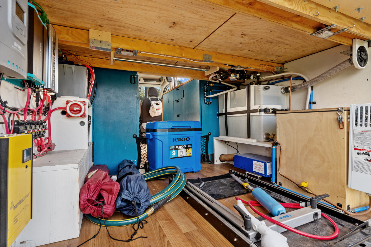 RV rental utility bay showing electrical system (inverters, battery switch) and water tanks/plumbing for off-grid use.