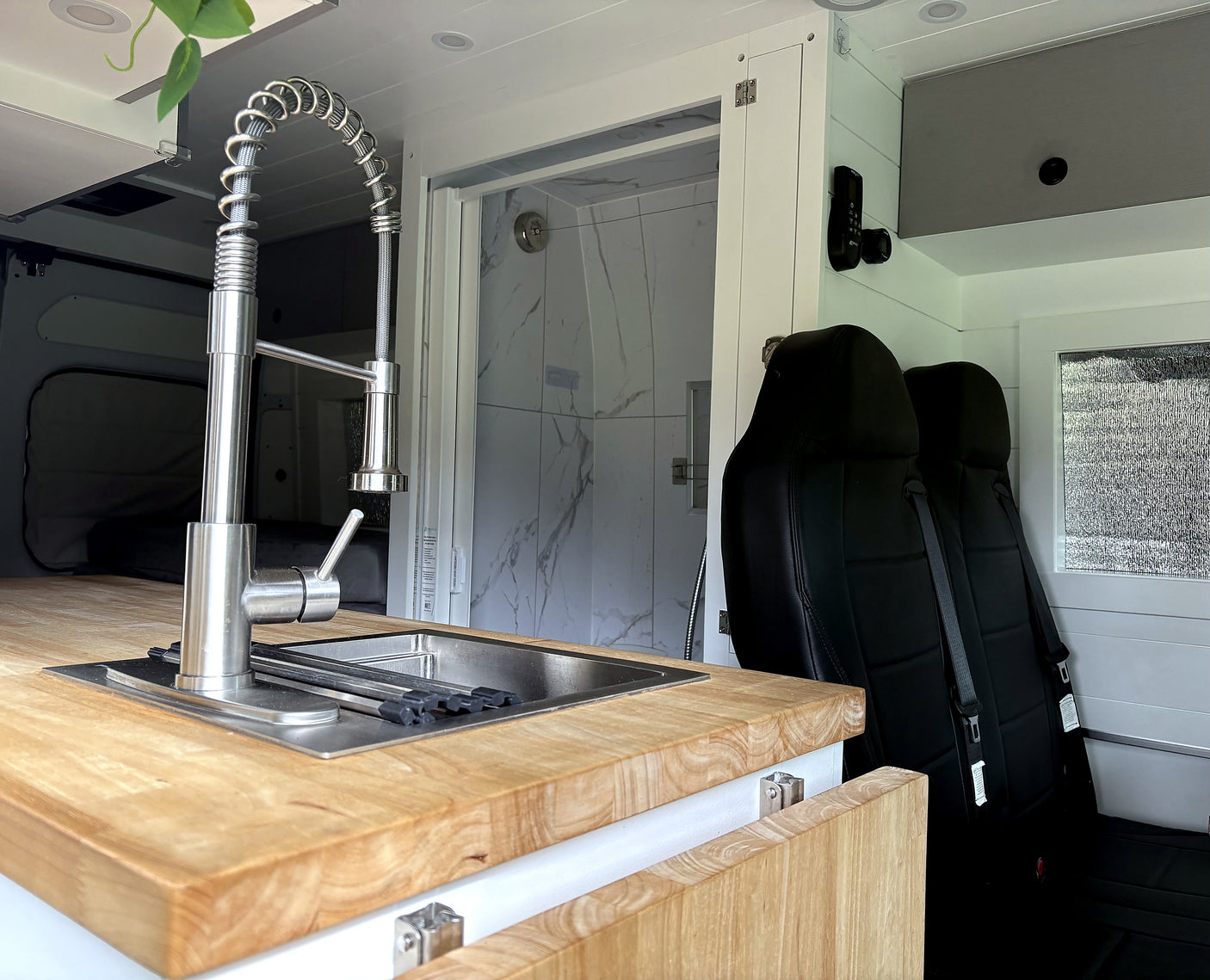 RV rental: Modern van conversion interior featuring a kitchen sink, shower, and rear passenger seats for comfortable travel.