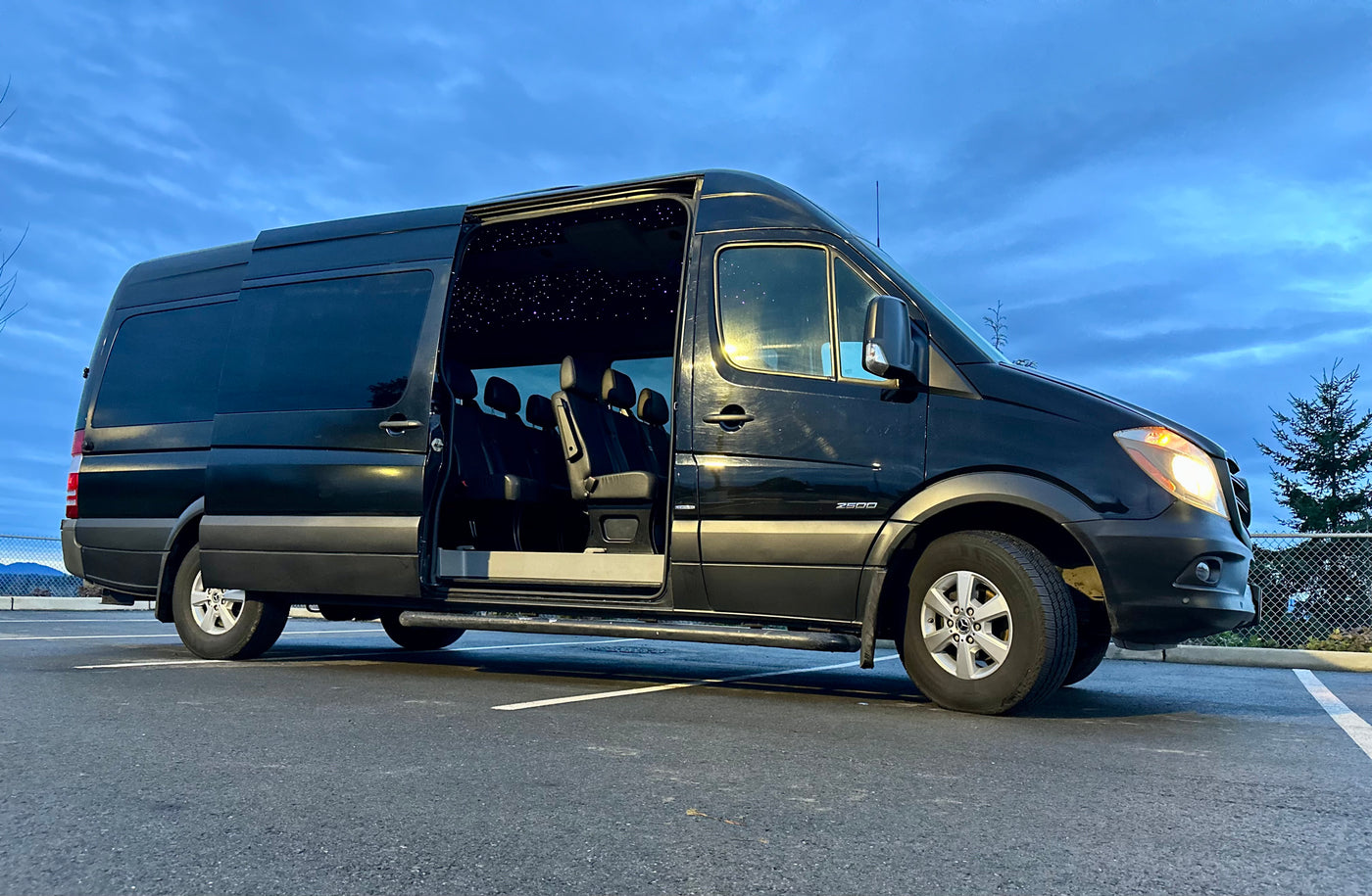 Black Mercedes Sprinter van for RV rental, showing plush interior seats & starry ceiling with side door open. — photo 5