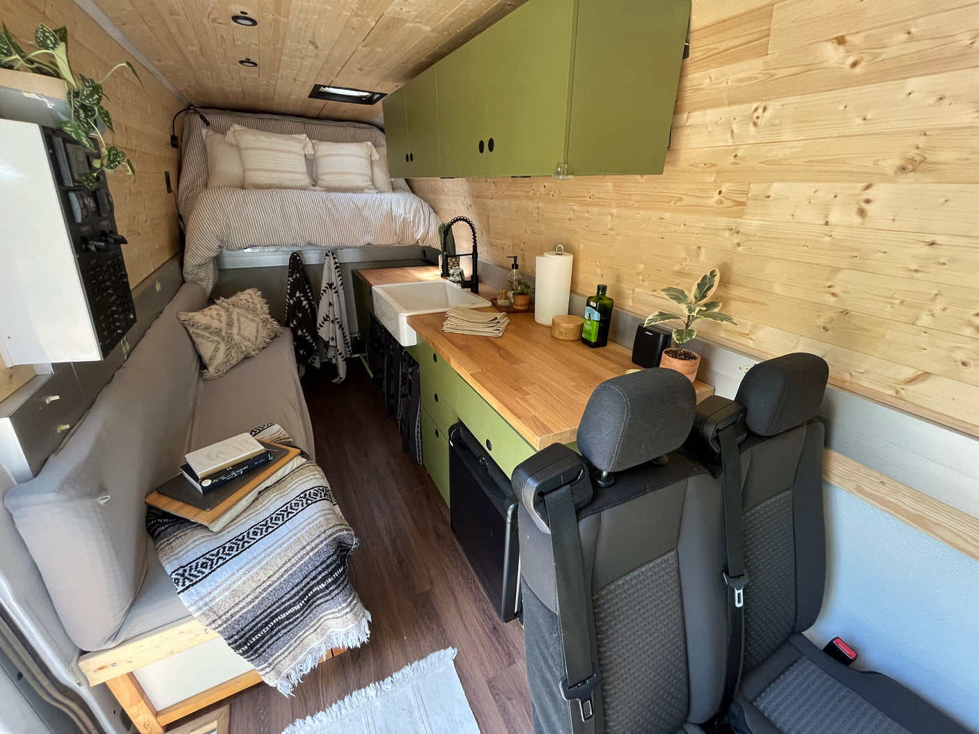Cozy camper van RV rental interior features a kitchen, bed, and wood paneling. Ideal for travel and adventure.
