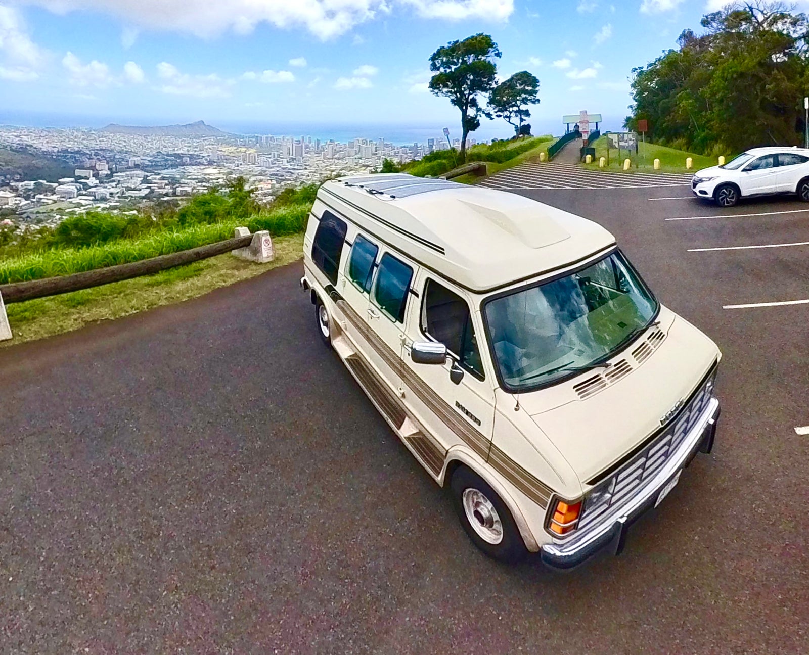 Cream camper van RV rental parked at a scenic Hawaii overlook, offering panoramic city and ocean views.
