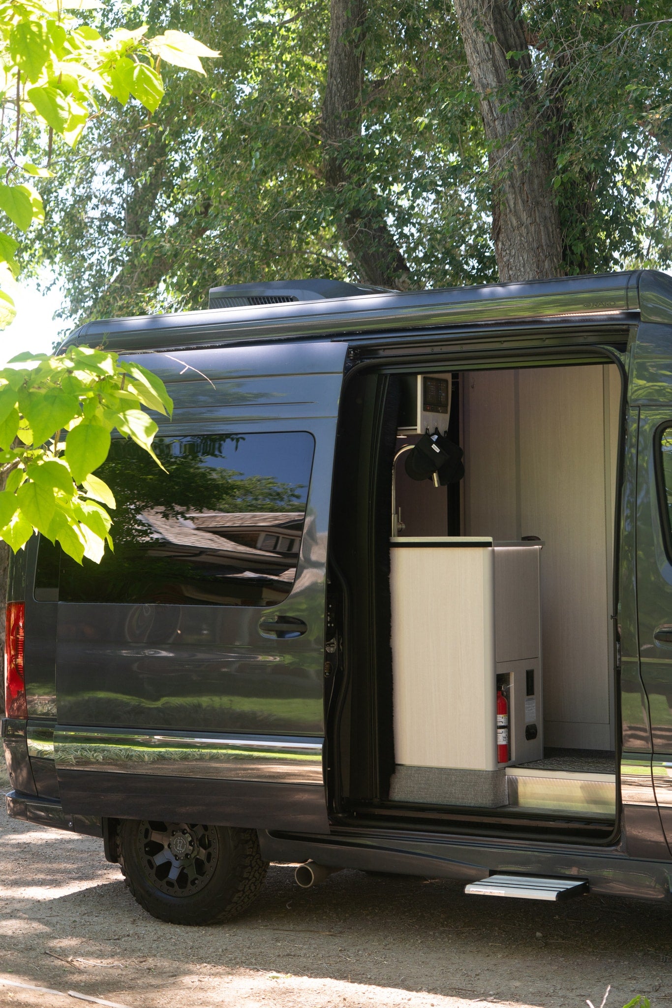 Dark grey RV rental with side door open, revealing a compact interior kitchen, fire extinguisher, and pull-out step, ready for adventure. — photo 7