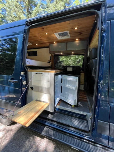 Tour an rv rental! See this custom camper van's interior: wood walls, built-in bed, and open fridge.