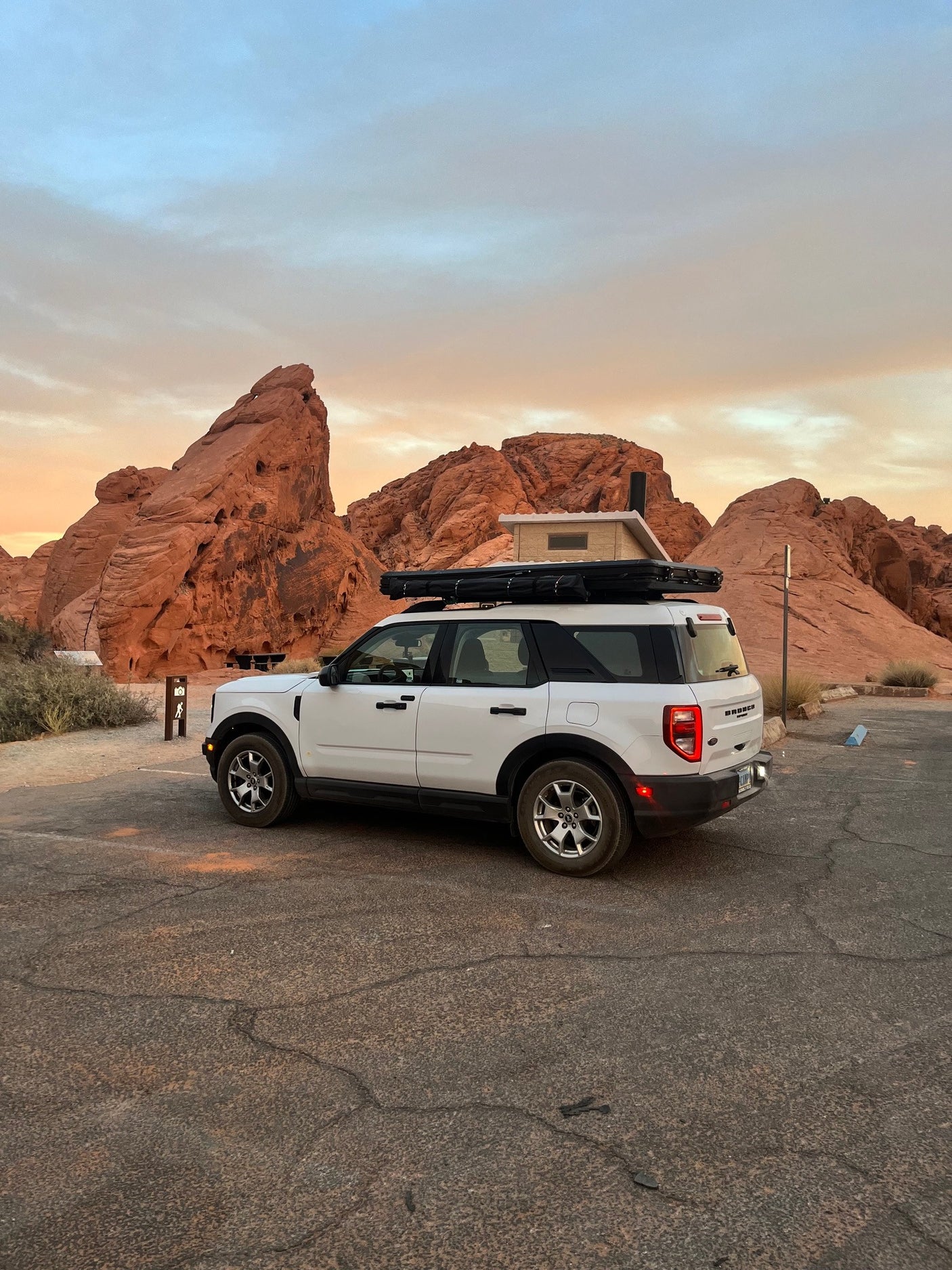 White Ford Bronco Sport with rooftop tent, a great RV rental for desert adventures among red rocks at sunset.