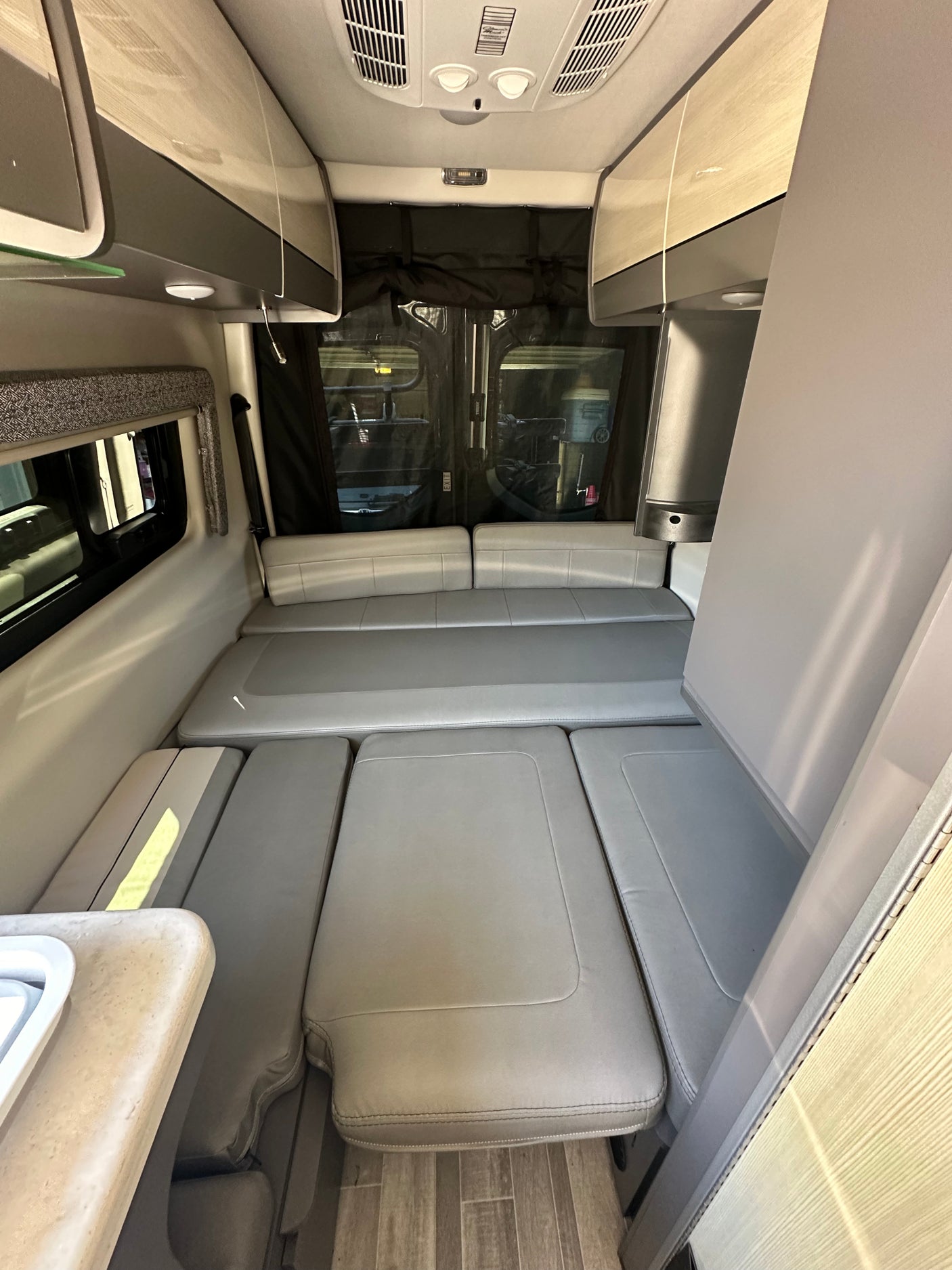 Interior view of a modern RV rental, featuring convertible light gray seating, overhead cabinets, and a side counter.