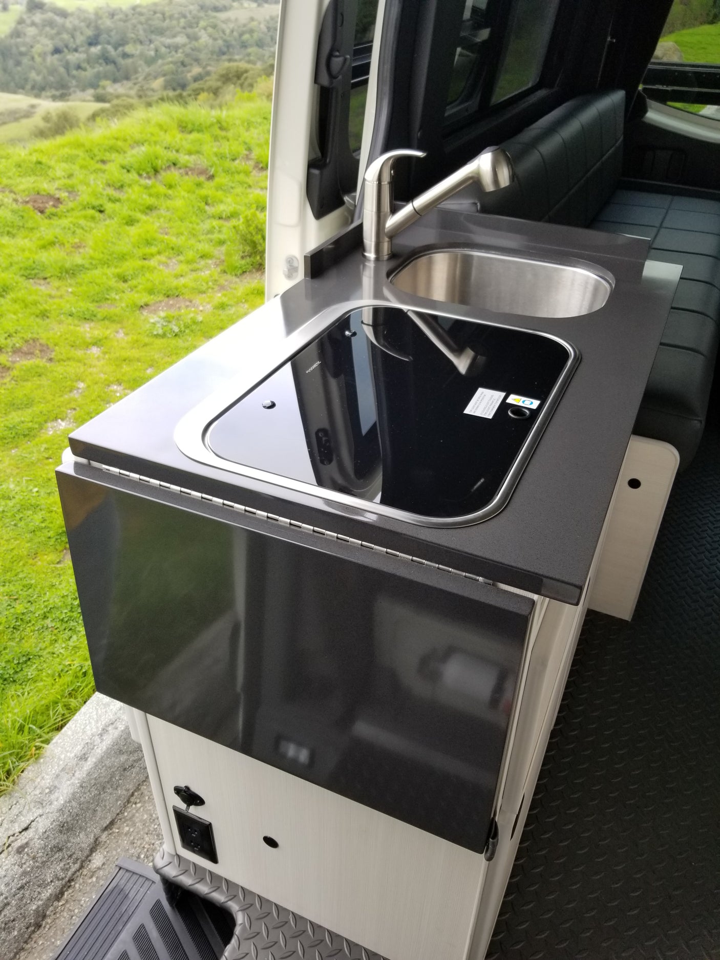 Modern **RV rental** galley kitchen with sink, cooktop, and folding counter, offering scenic outdoor views.