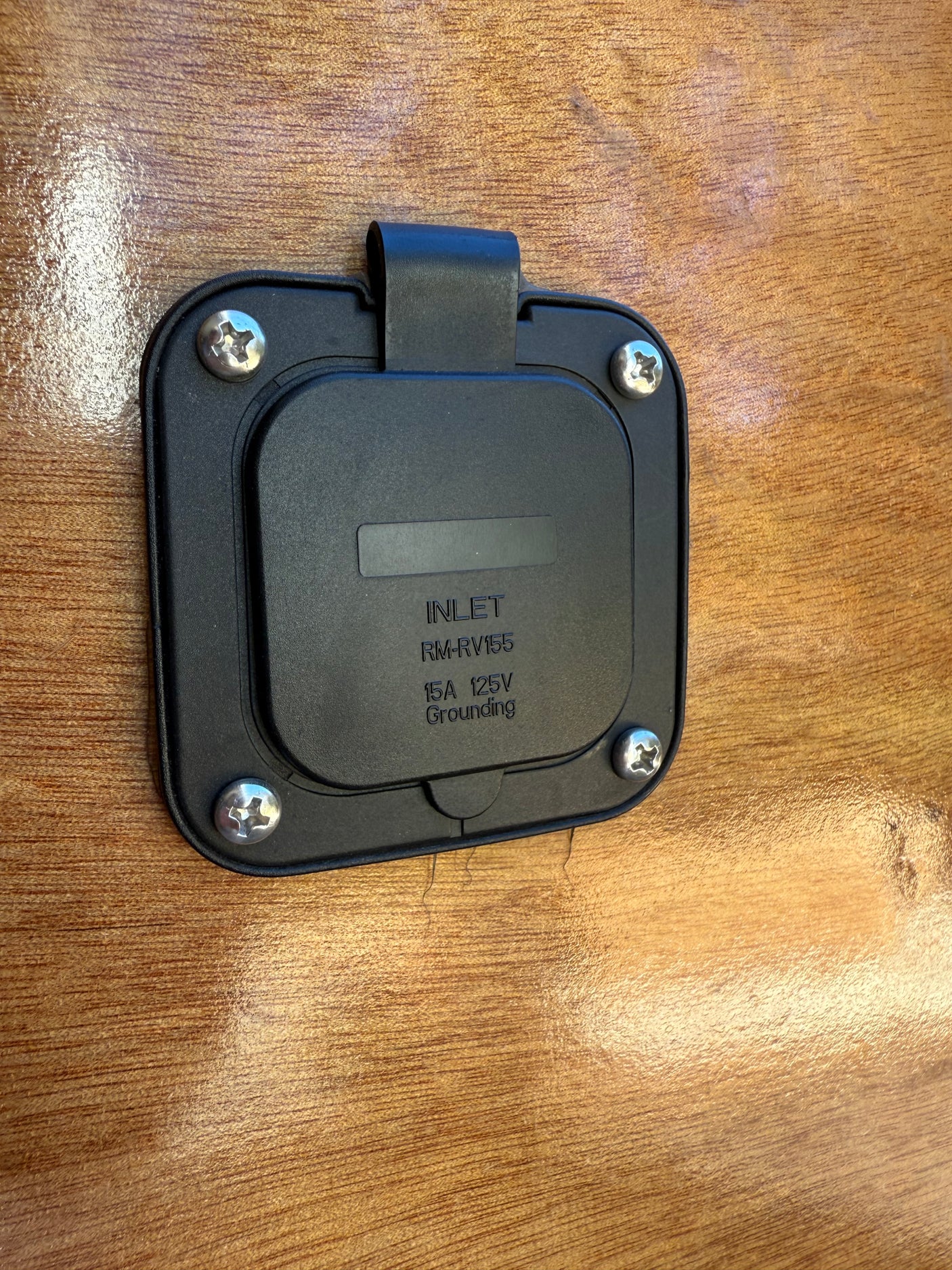 Black 15A 125V RM-RV155 electrical shore power inlet on a wooden wall, essential for an RV rental hookup.
