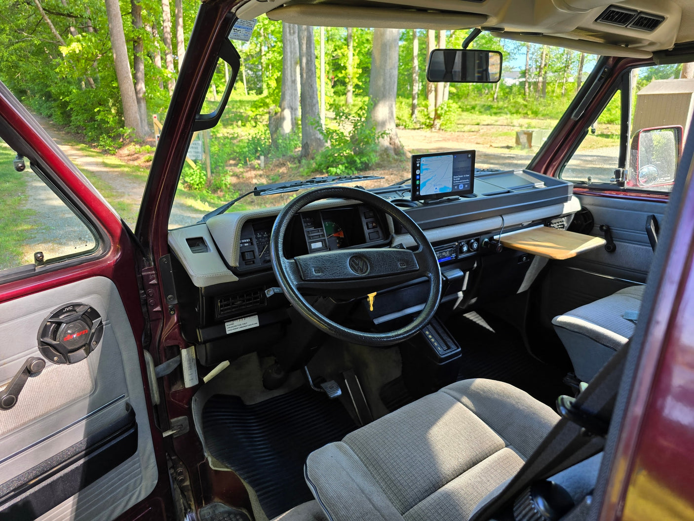 is parked on a gravel path by a serene lake with docks and lush trees.|Relaxing by the river: a maroon camper van