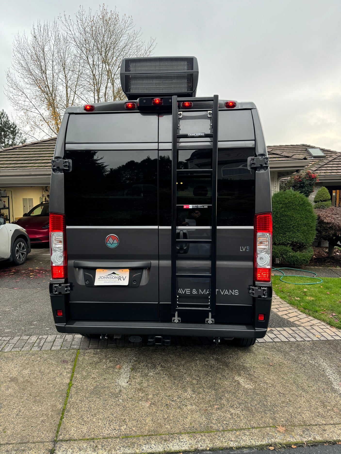 Rear view of a grey camper van with a roof AC unit and ladder, featuring custom branding. Great for an rv rental.