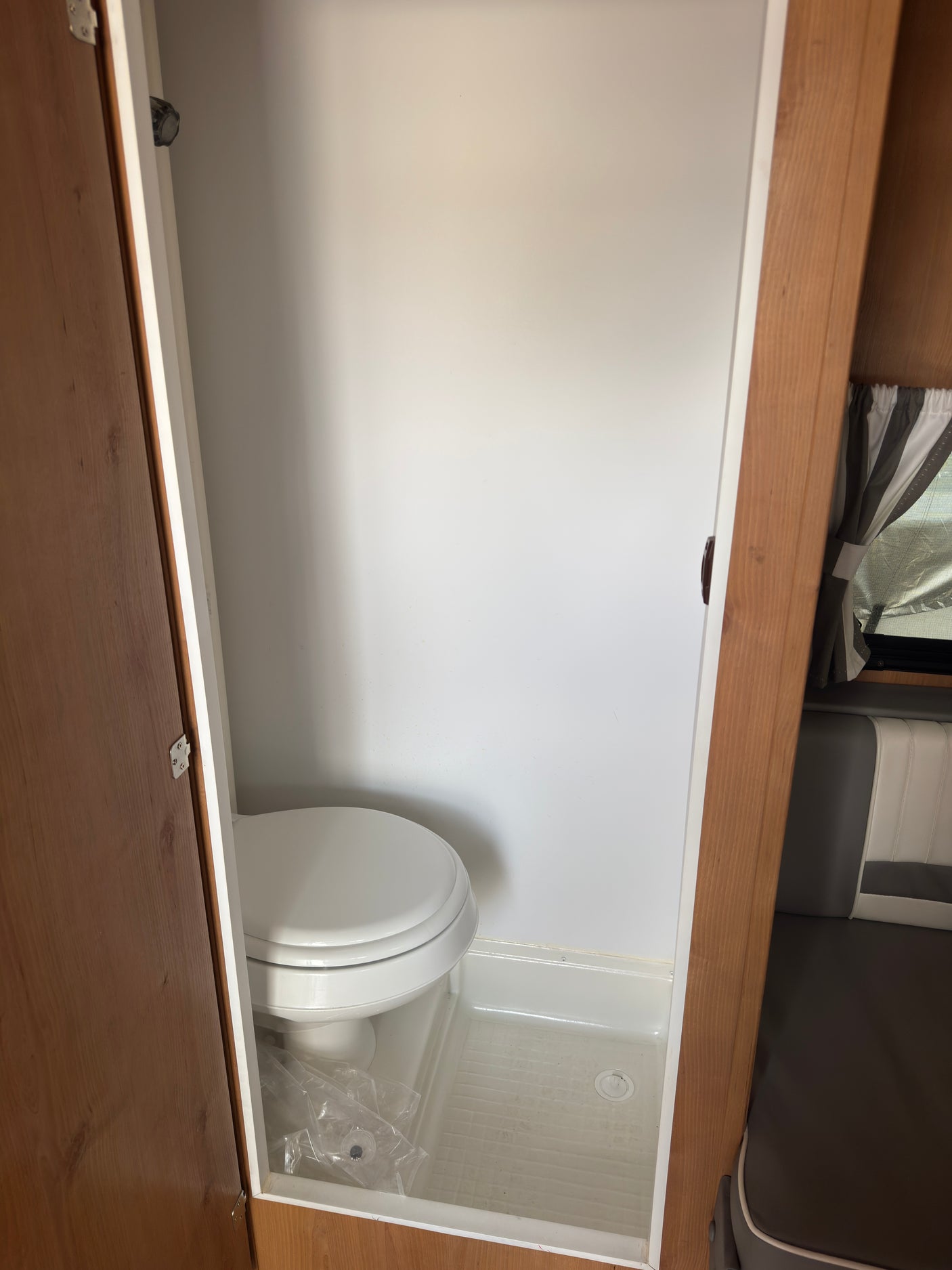 RV rental: Compact RV bathroom with a white toilet and integrated shower pan within a narrow, light-colored stall.
