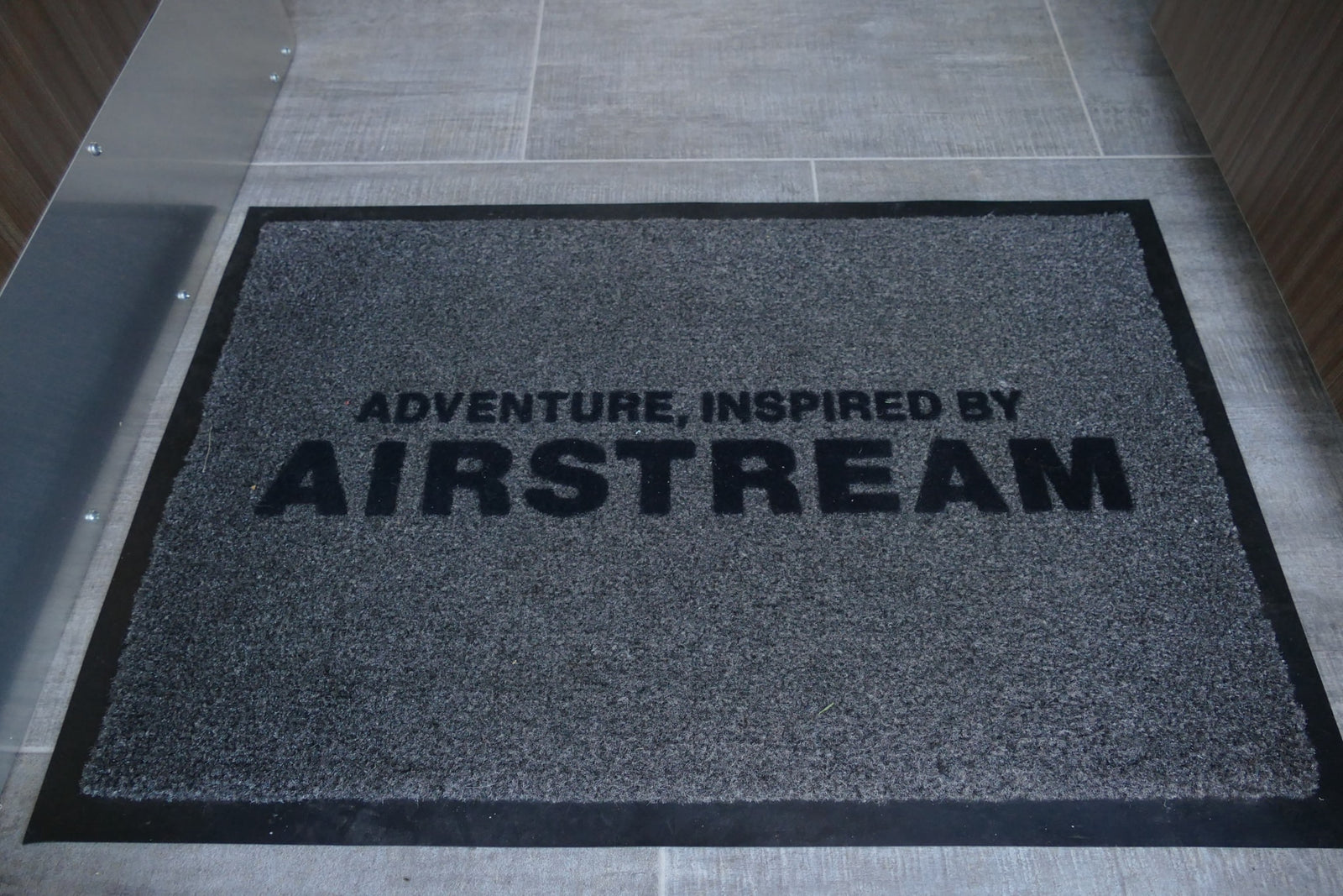 Inside an RV rental, a grey Airstream welcome mat reads 'ADVENTURE, INSPIRED BY AIRSTREAM' on a tiled floor.