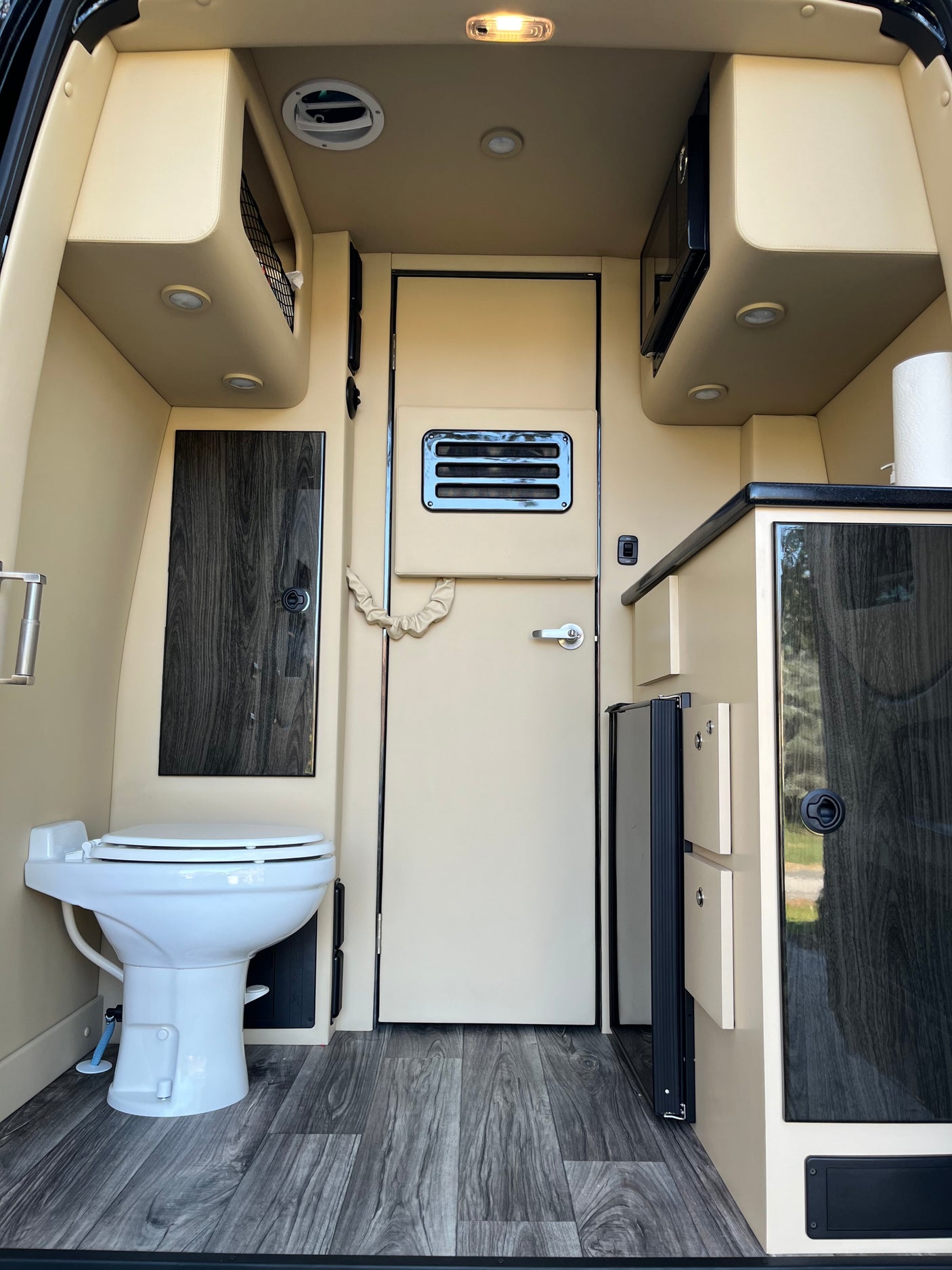 Interior of an RV rental, featuring a compact bathroom with toilet, a well-equipped kitchen with microwave, and integrated storage.