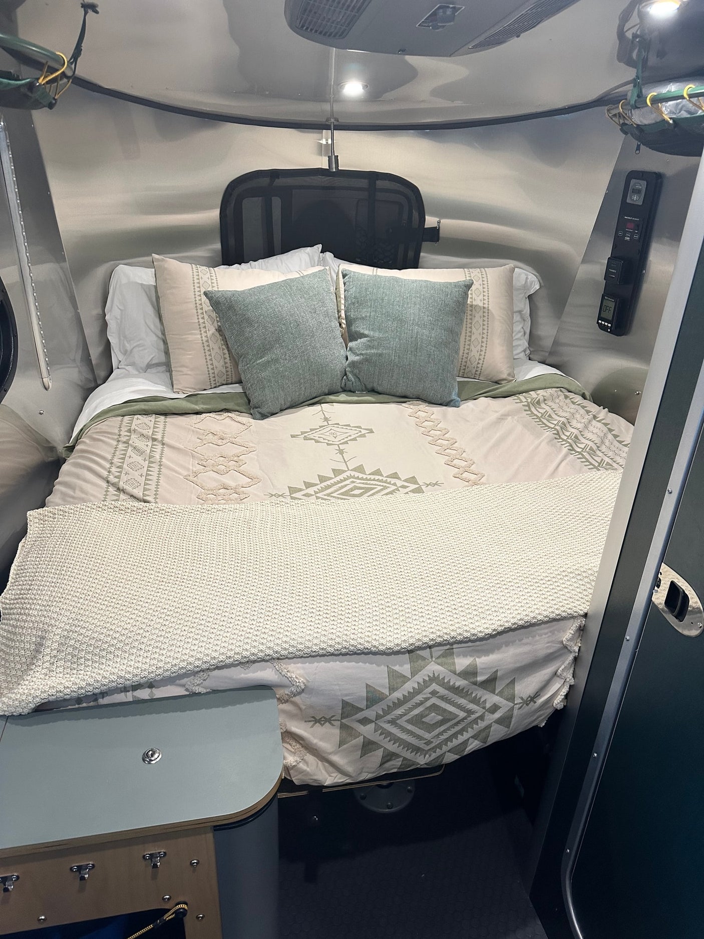 Cozy RV rental bedroom with patterned bed linens, teal pillows, and sleek, compact camper interior for comfortable travel.