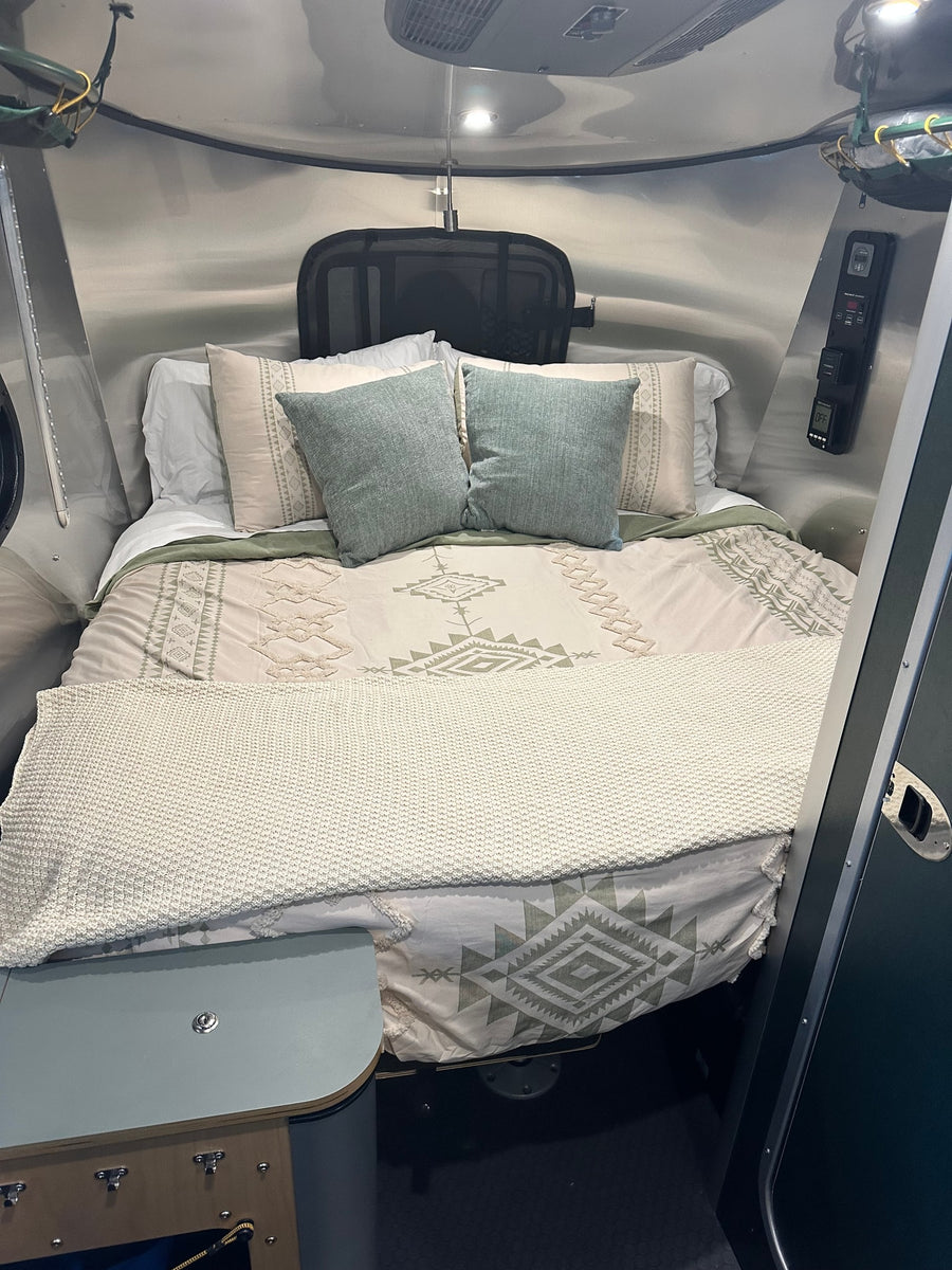 Cozy RV rental bedroom with patterned bed linens, teal pillows, and sleek, compact camper interior for comfortable travel.