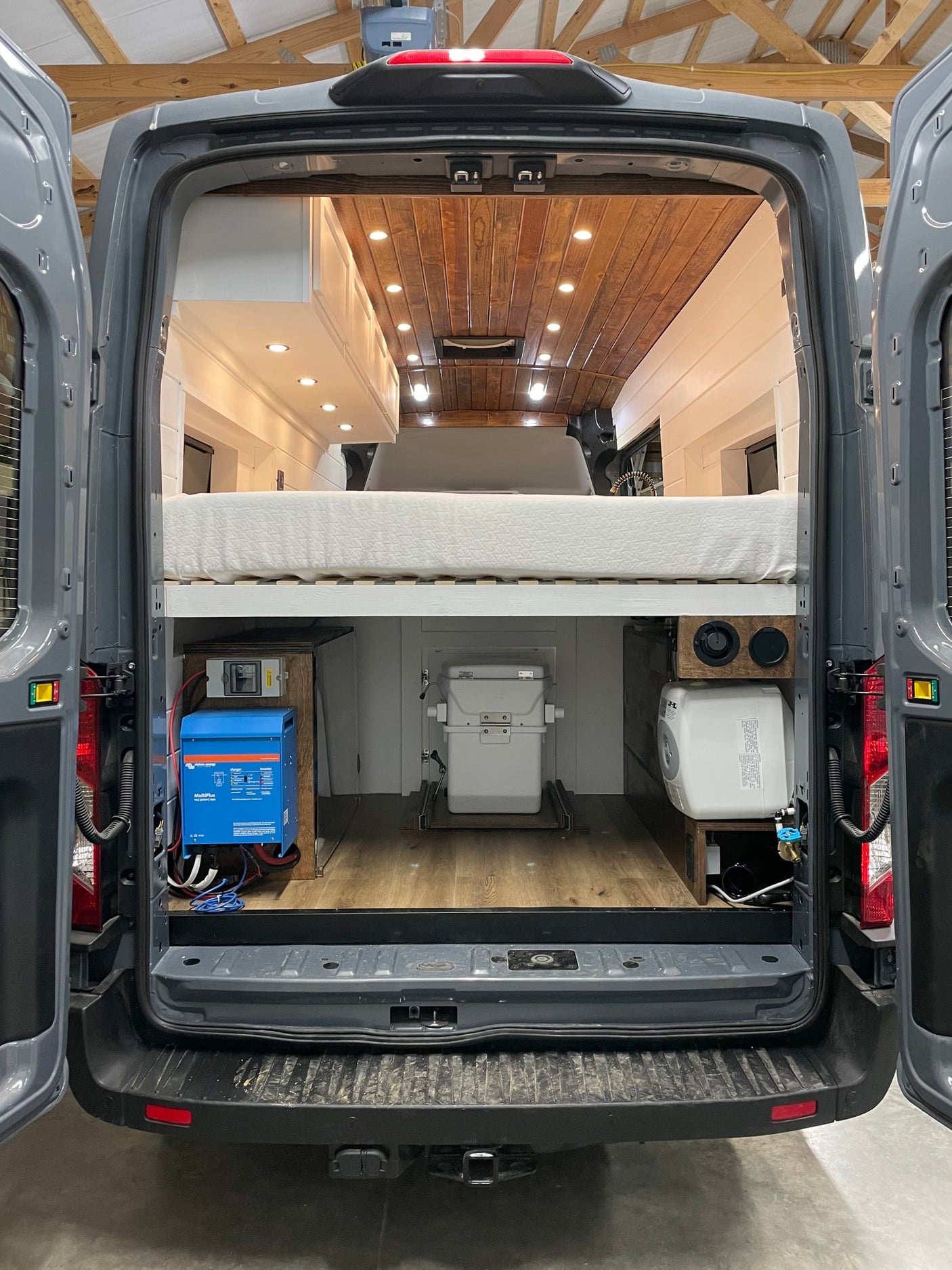 Inside this custom gray camper van RV rental: a comfortable bed, Victron power system, slide-out toilet, and water heater.