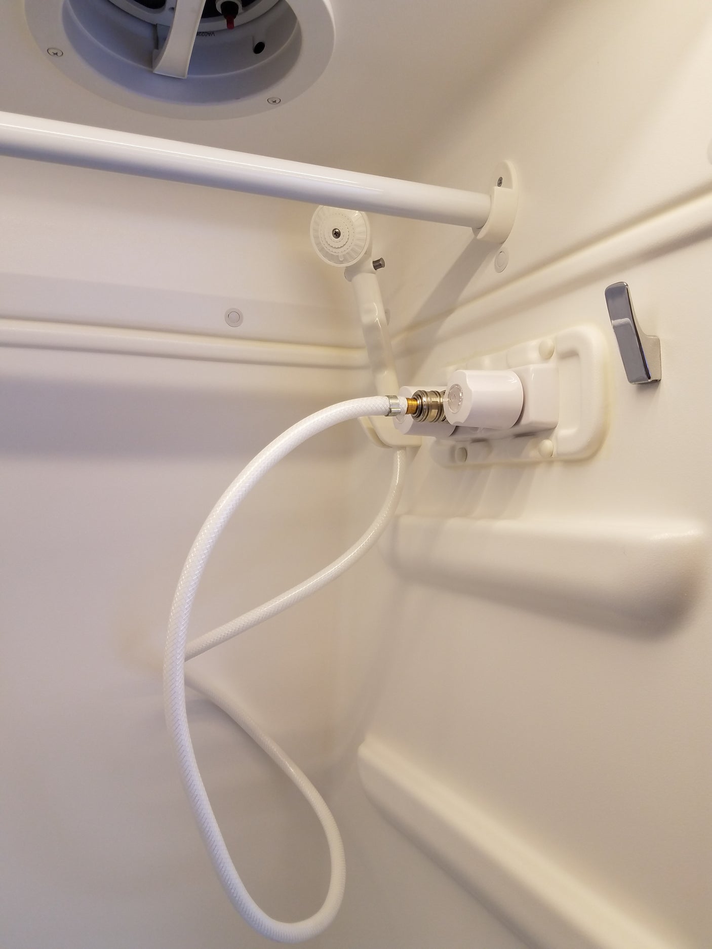 RV rental compact shower interior, with a hose, detached shower head, fixtures, and ceiling vent.