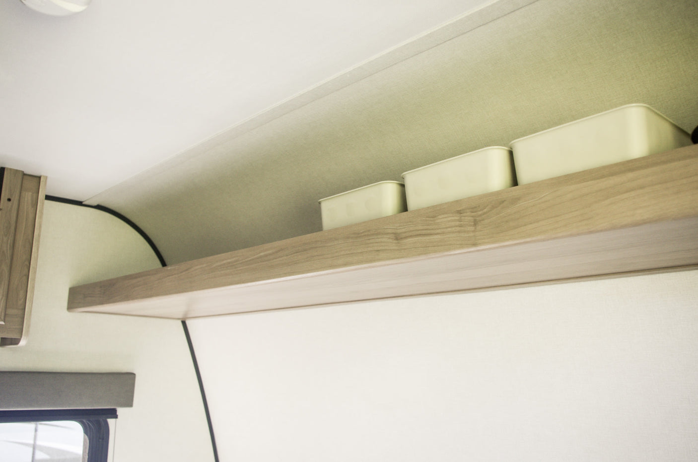 RV rental cabin interior features a light wood shelf with three pale storage bins. Above are curved light-colored panels.