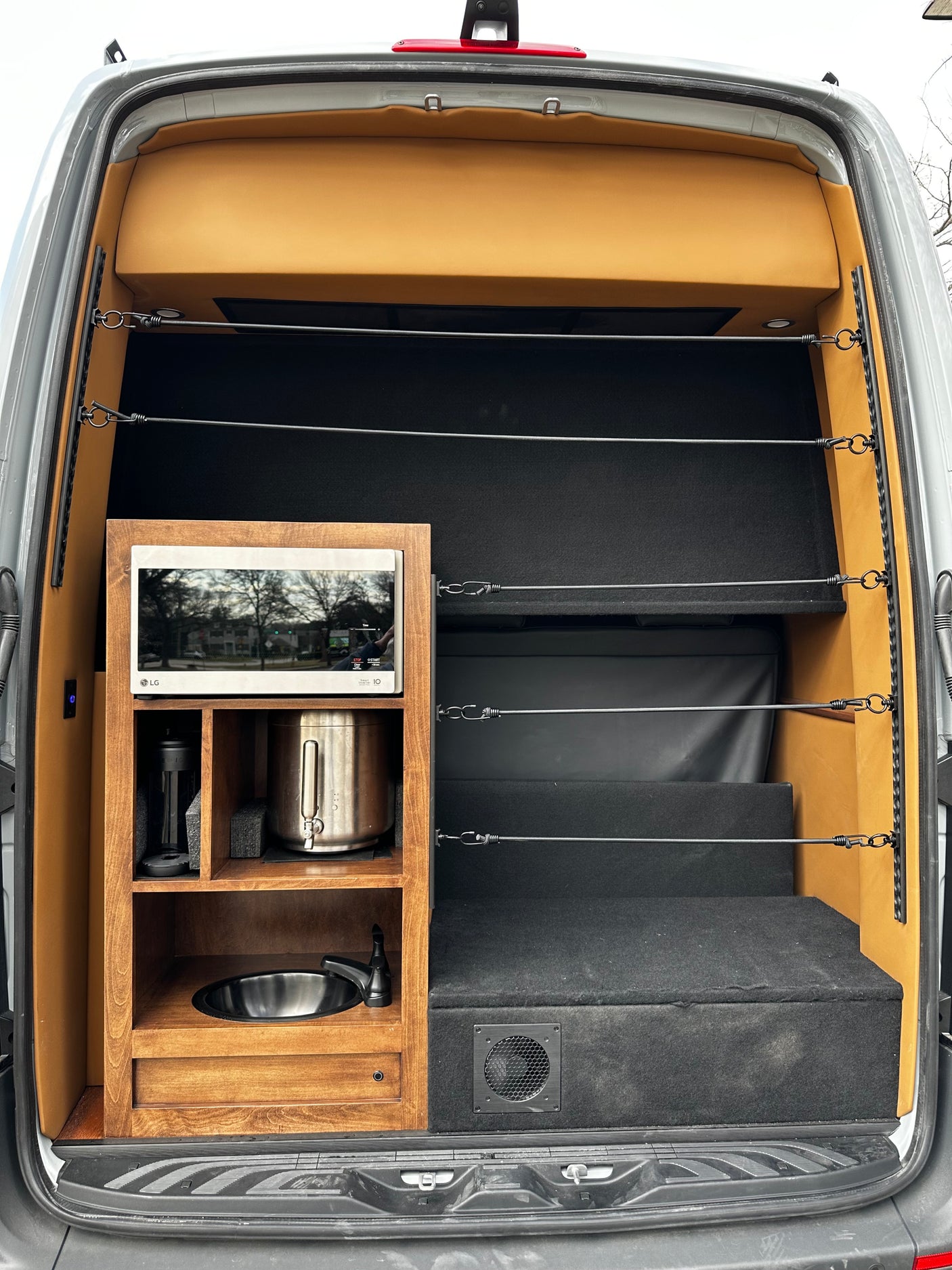 RV rental camper van with a built-in kitchenette (sink, microwave, coffee maker) and a modular bed/storage area inside.