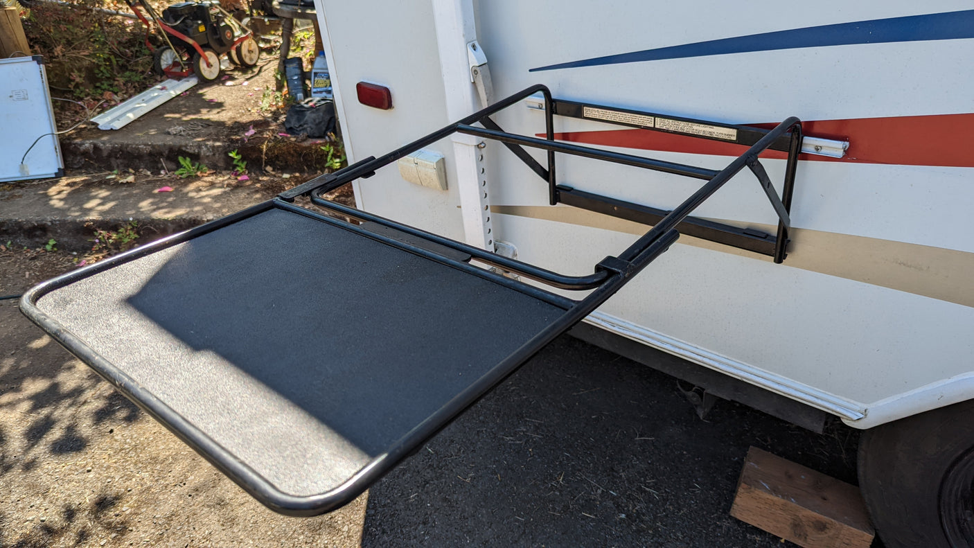 An outdoor black table, an ideal RV accessory, folds out from the side of a white RV for your rv rental adventure.