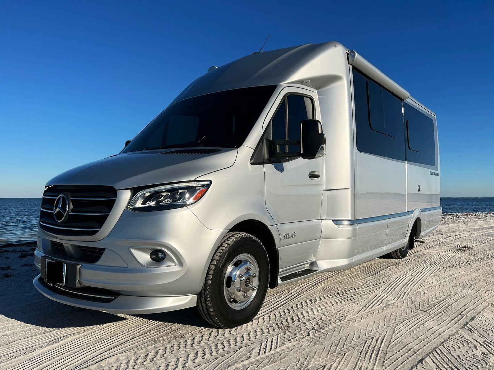 Silver Airstream Atlas RV rental, a luxury Mercedes-Benz camper van, gleaming on a sun-drenched beach.