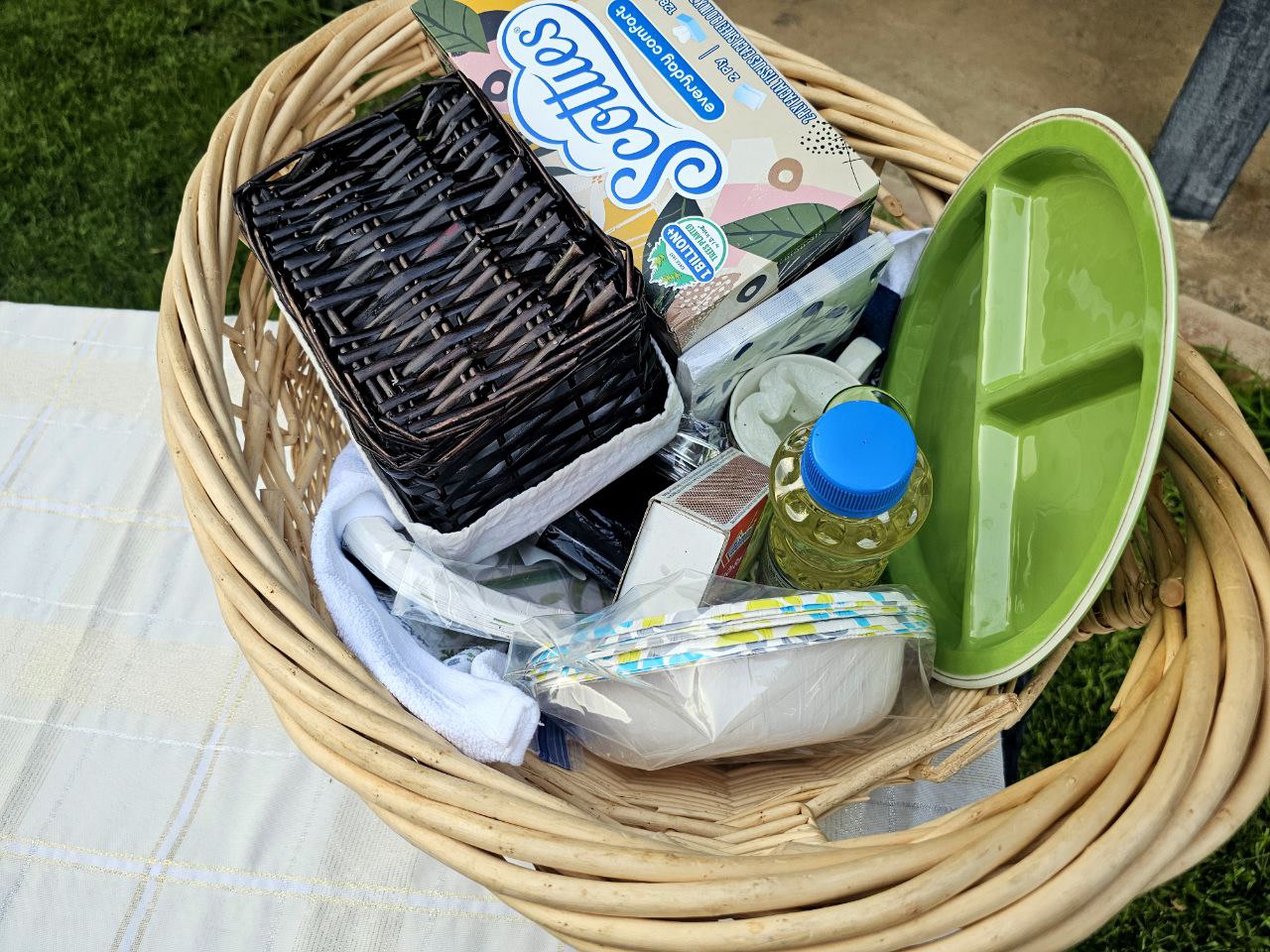 Wicker basket packed with RV rental trip essentials: Scotties tissues, paper bowls, a green plate, and other picnic supplies.