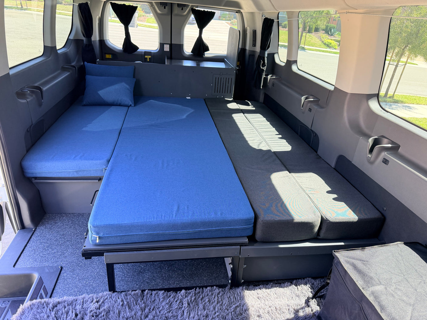RV rental: Inside a camper van with a cozy bed featuring blue and grey cushions, ready for travel and adventure.