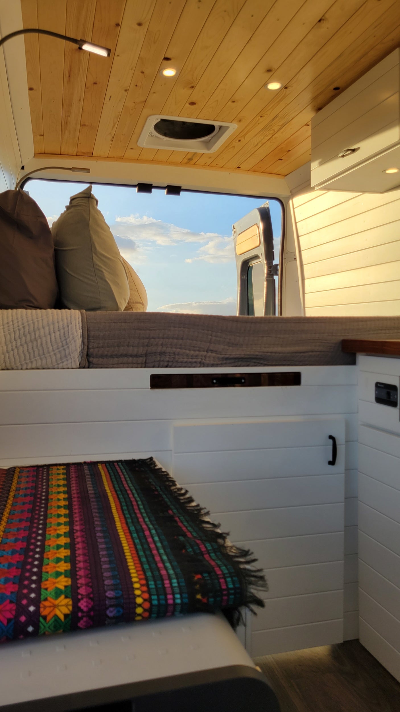This RV rental offers a bright, cozy interior. Wooden ceiling, comfy bed, and open back doors reveal a beautiful sky.