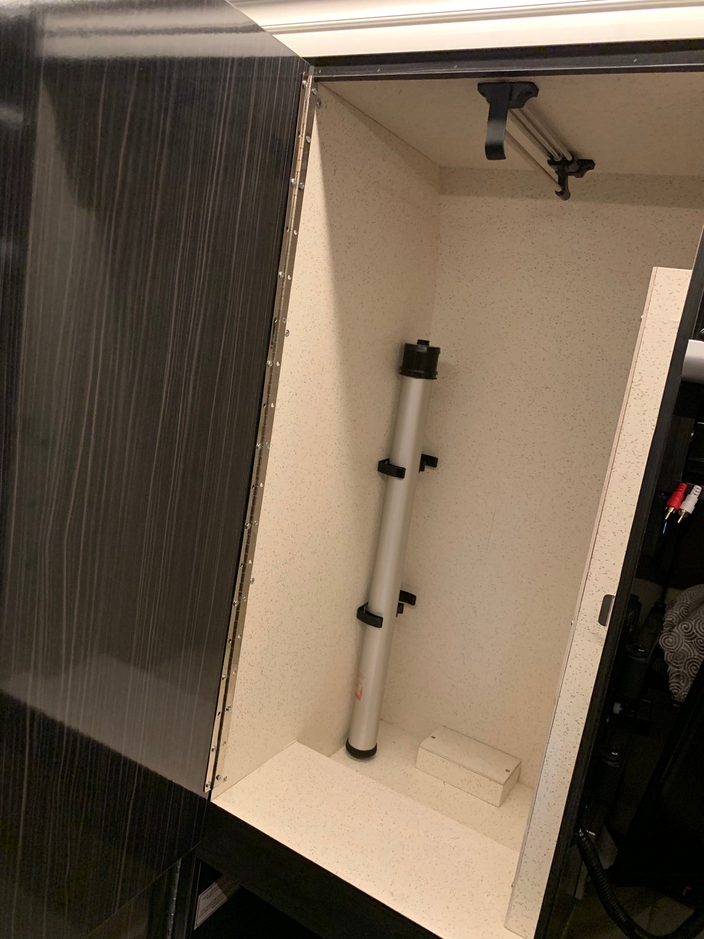 Organized RV rental storage cabinet features a light speckled interior, telescopic pole, and pull-out hanging bar.