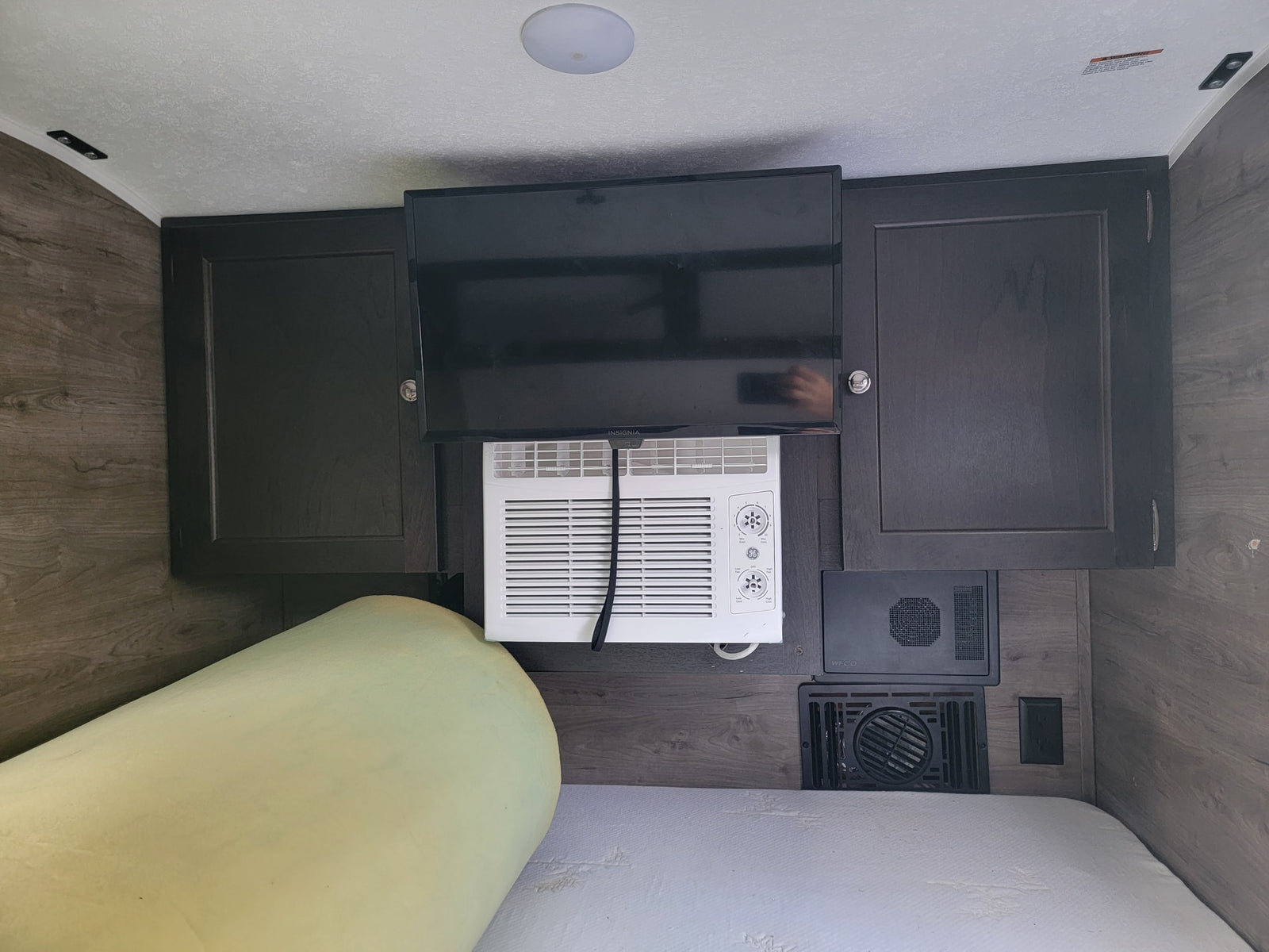 Inside an RV rental bedroom: mounted TV, window AC unit, wood-look cabinets, and a comfortable bed.