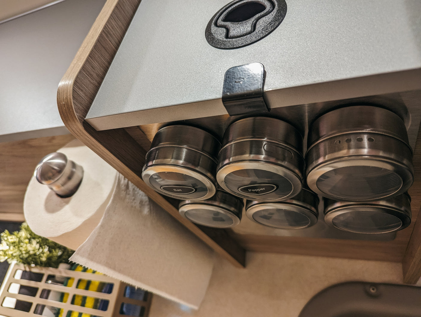Maximize space in your RV rental! Organized compact kitchen with magnetic spice jars mounted under a cabinet, and a paper towel roll below.