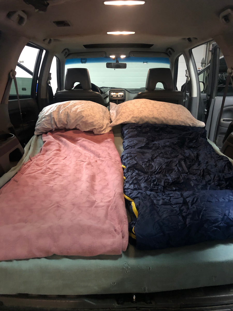 View inside a car, transformed for car camping with two sleeping spots, pillows & blankets. Great for a budget RV rental trip!