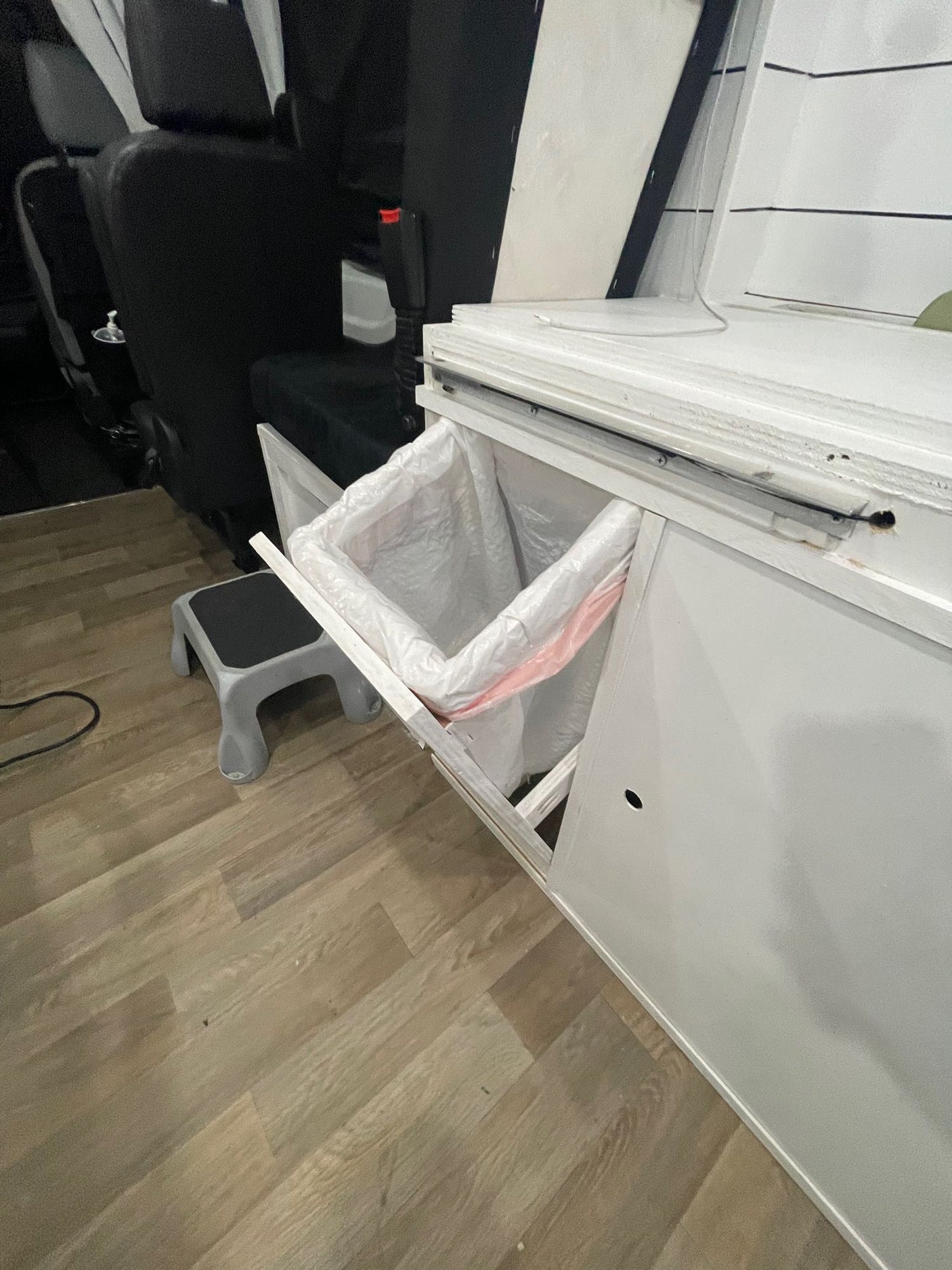 RV rental: Compact van interior with open pull-out trash, black seats, wood floor, and step stool for convenience.