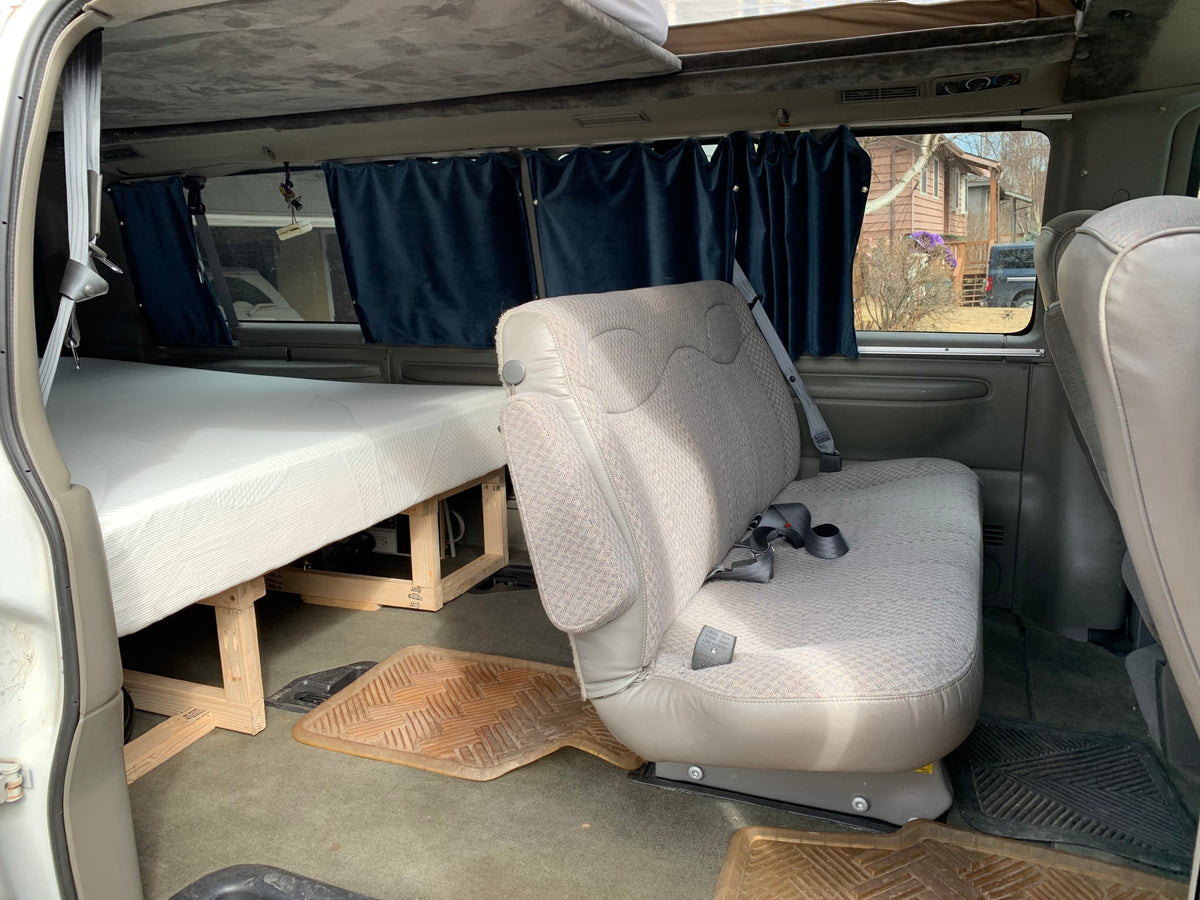 Van RV rental interior: cozy bed with wooden frame, privacy curtains, and passenger seating for road trips. — photo 5