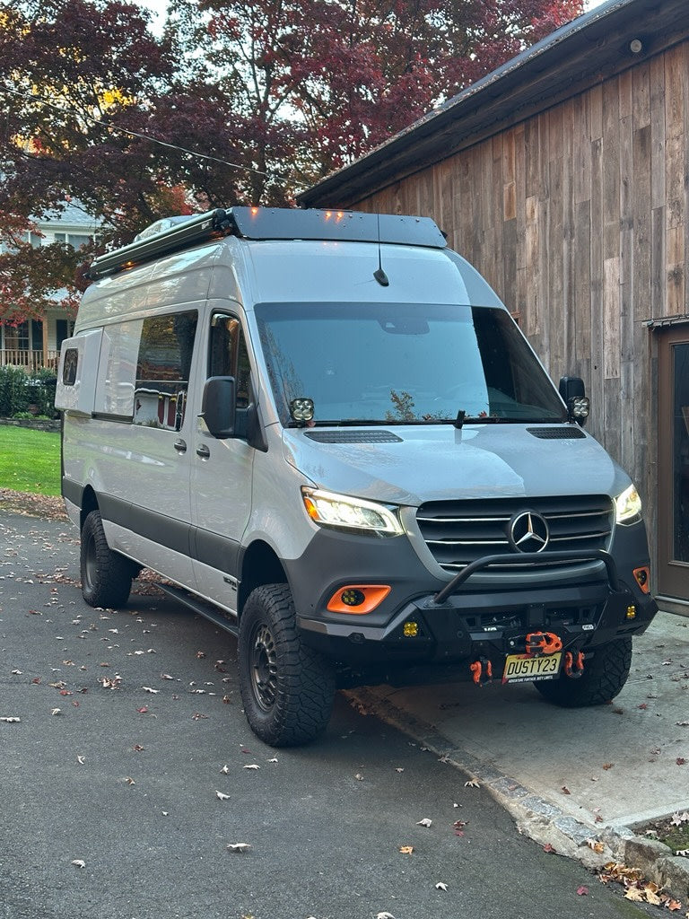 Custom Mercedes Sprinter van on an asphalt driveway. This adventure-ready rv rental features off-road tires