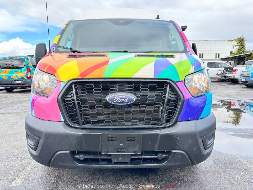 Front of a vibrant, rainbow-wrapped Ford Transit van, likely an rv rental, parked in a wet lot.
