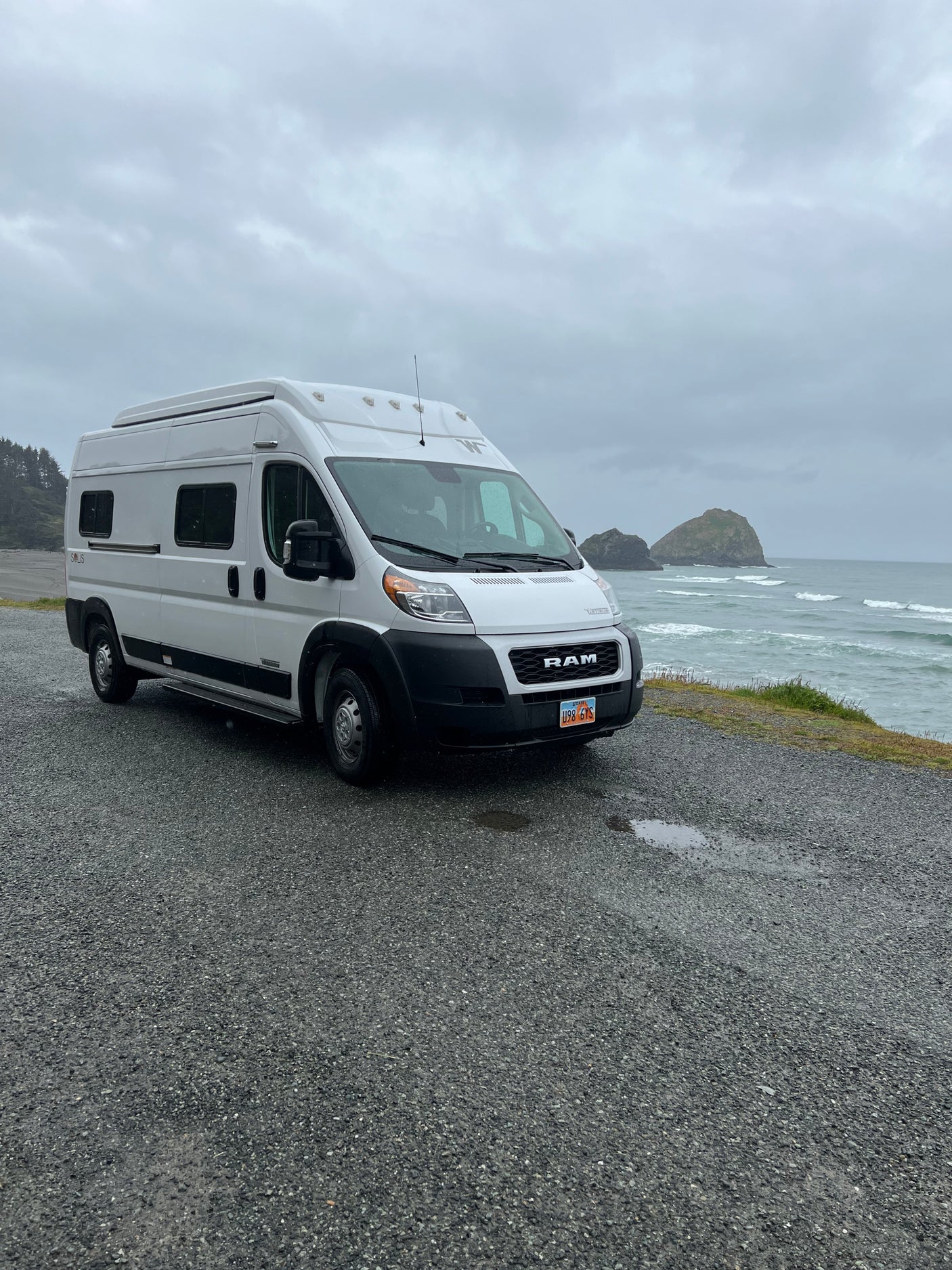 White Winnebago Solis RV rental parked on a gravel lot overlooking the stormy Pacific Ocean and sea stacks.