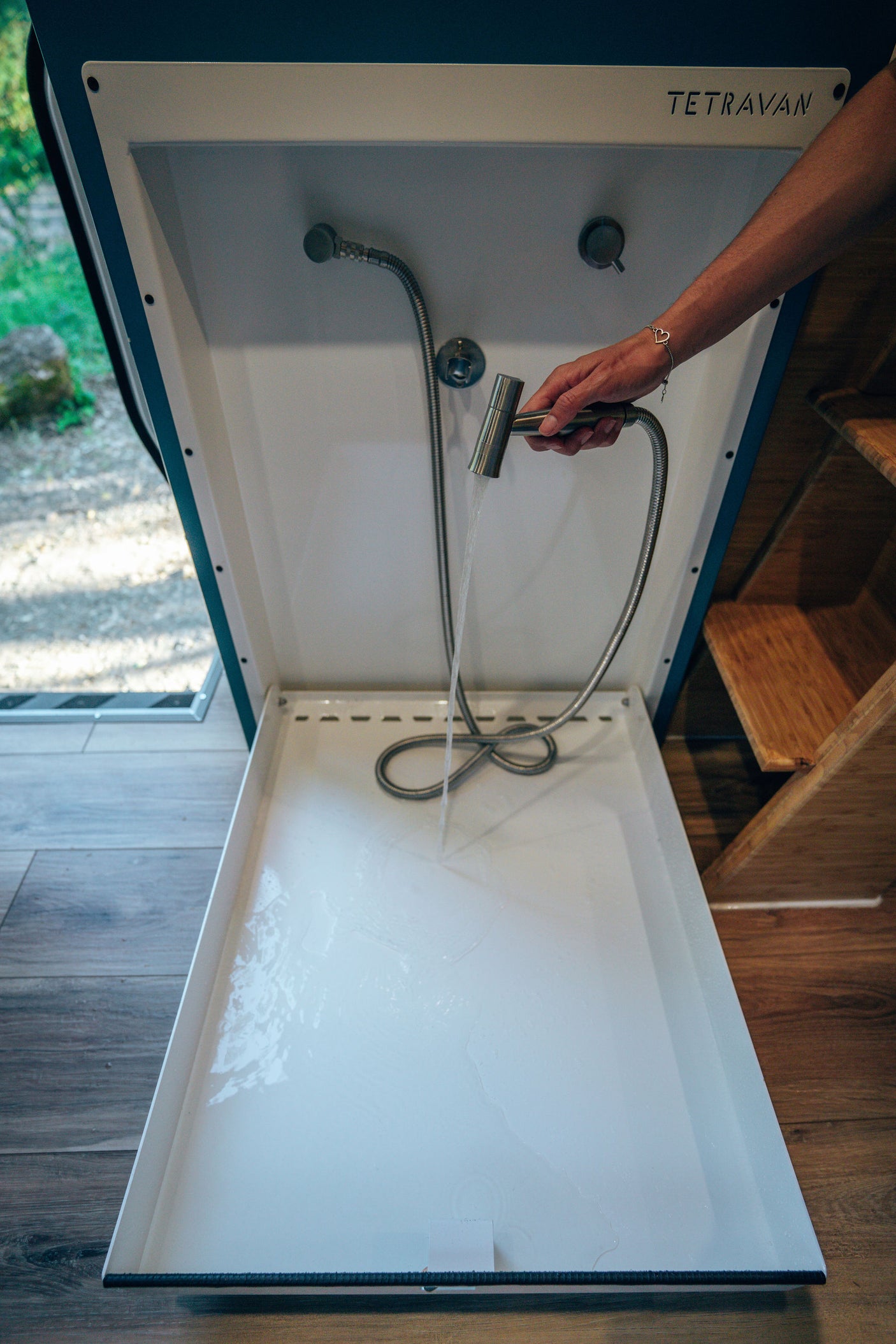 RV rental: Inside a Tetravan, a person demonstrates the compact shower with a handheld spray and water in the tray.