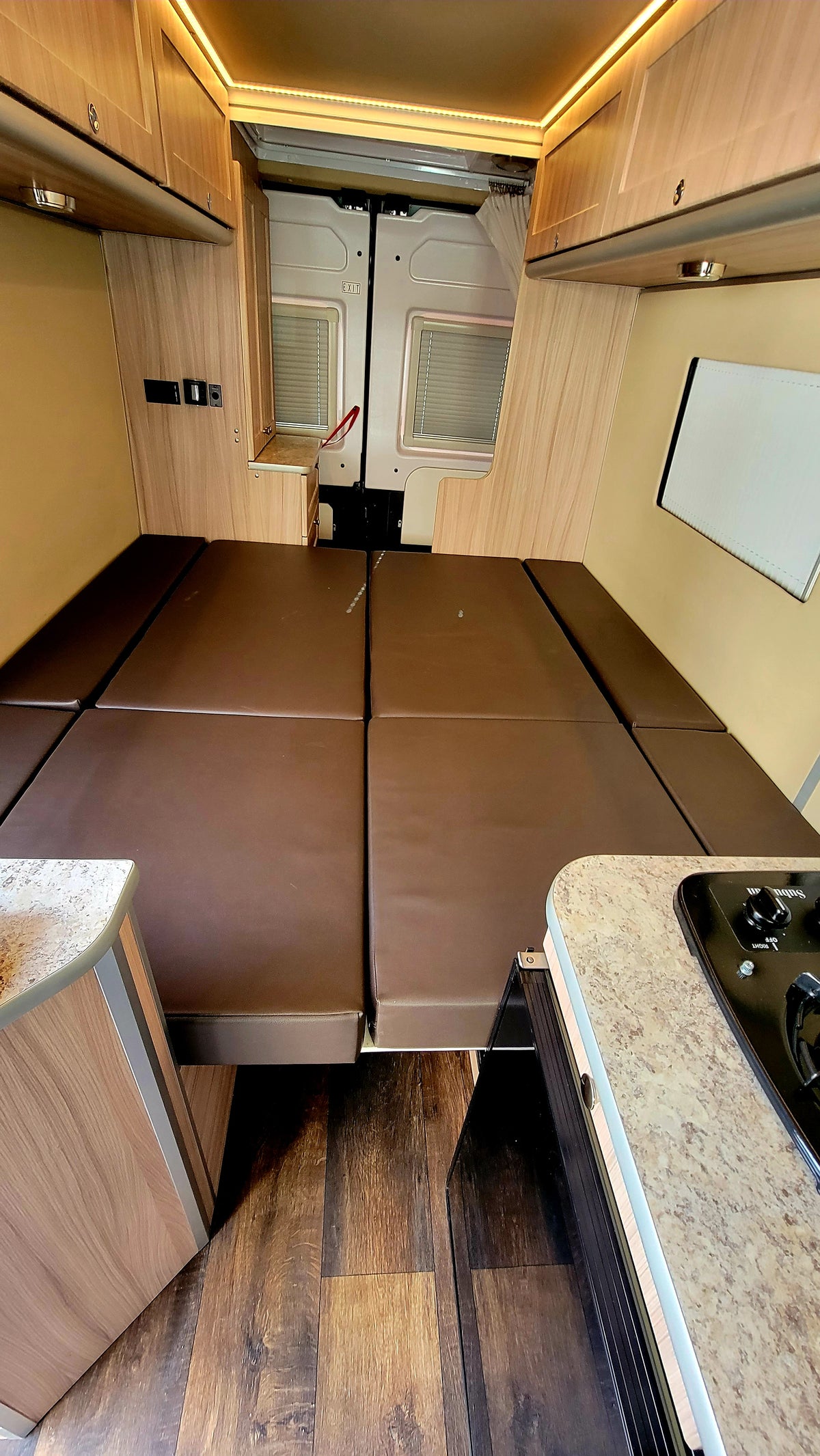 Camper van rv rental: functional interior with a large brown bed, wooden cabinets, and a convenient kitchen. — photo 16