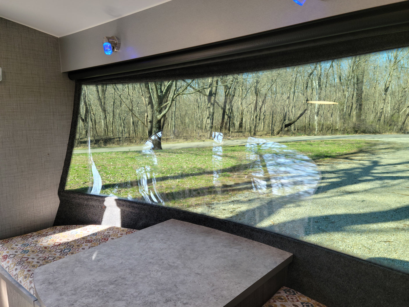 Enjoy the view from your RV rental! Cozy dinette with a large window overlooking a wooded outdoor scene.