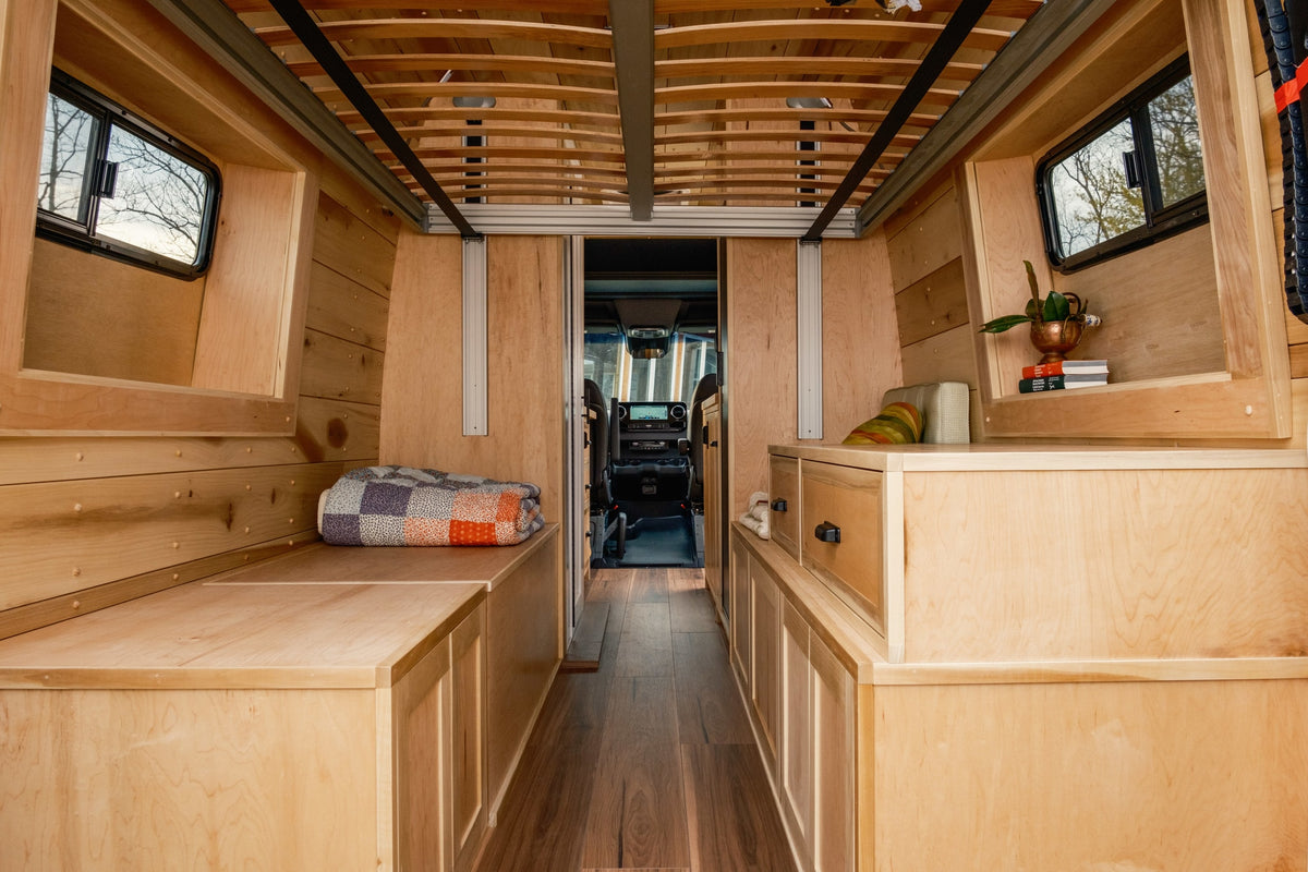 Step inside this cozy rv rental camper van, featuring a beautiful wooden interior with built-in storage, sleeping areas, and a view to the cockpit. — photo 9