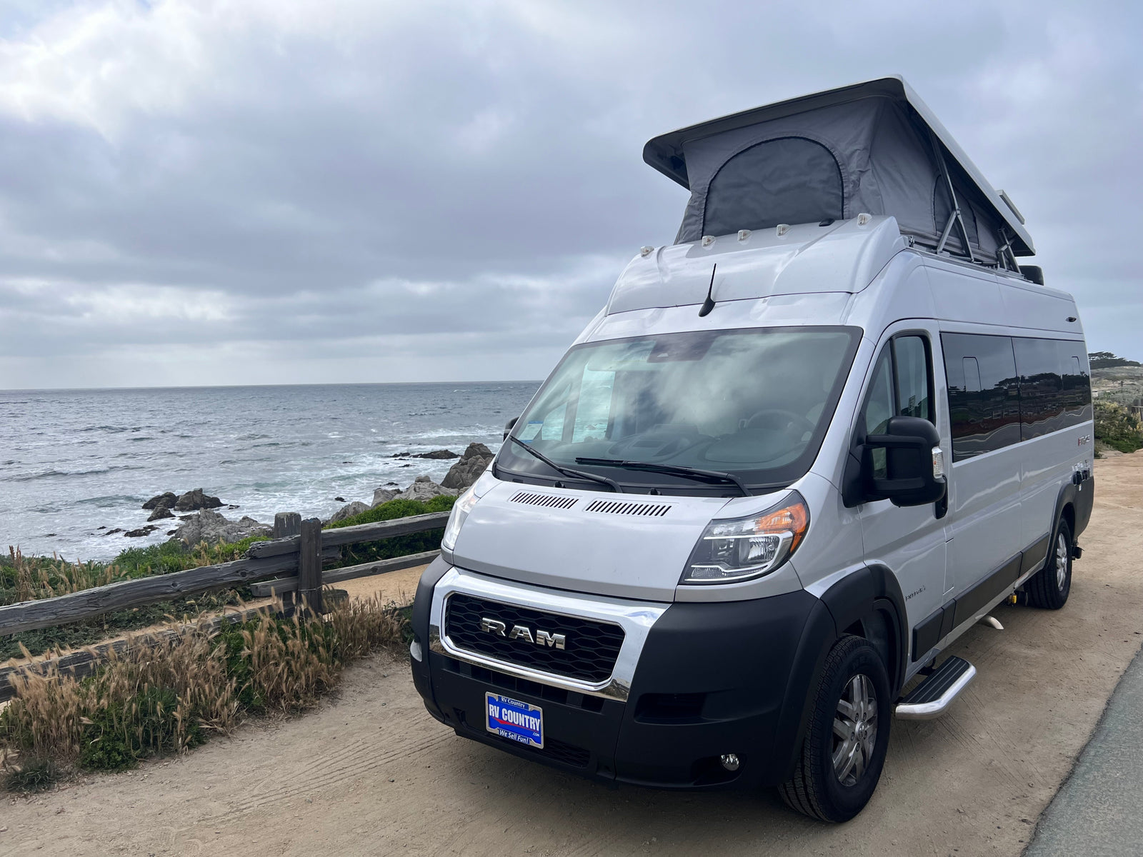 Silver Ram ProMaster camper van with pop-top for an RV rental parked by the ocean. Ideal for coastal travel.