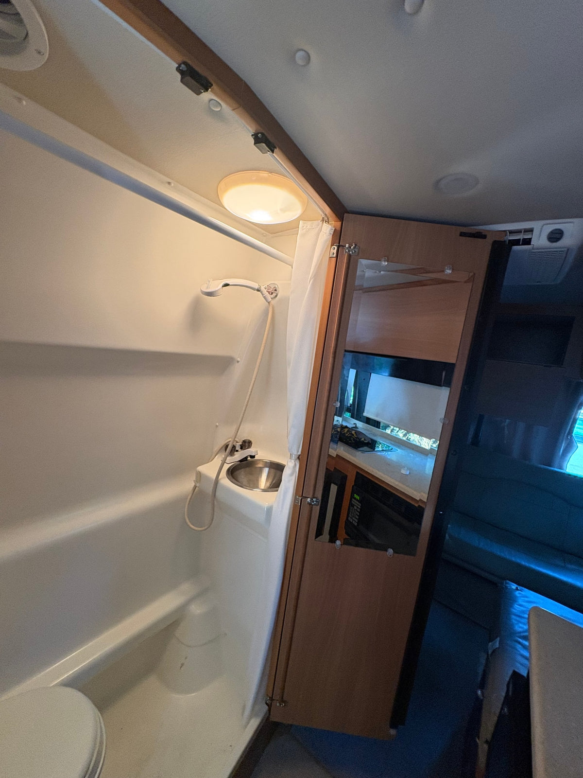 This rv rental features a compact bathroom with shower, toilet, and sink, reflecting the kitchen/living area in its mirror. — photo 9