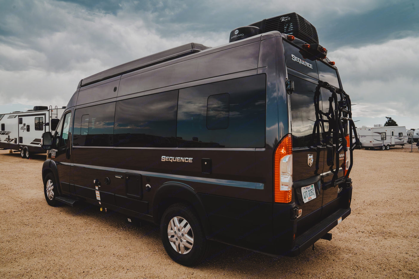 This dark camper van RV rental, a Thor Sequence, is parked on a gravel lot under a cloudy sky, ready for a road trip.