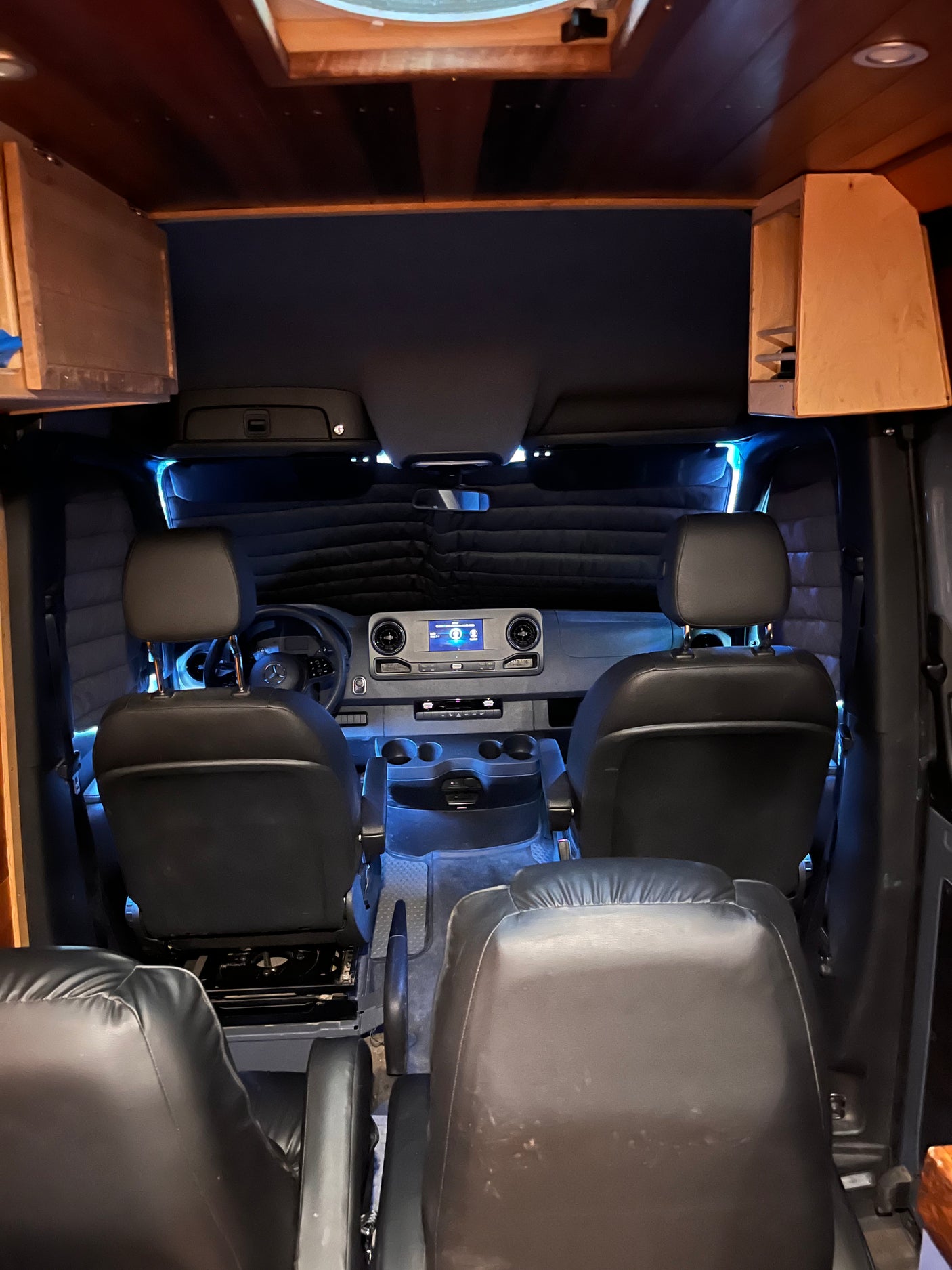 Experience comfort in this RV rental camper van. View of customized front cabin, dashboard, and swivel seats with blue lighting.