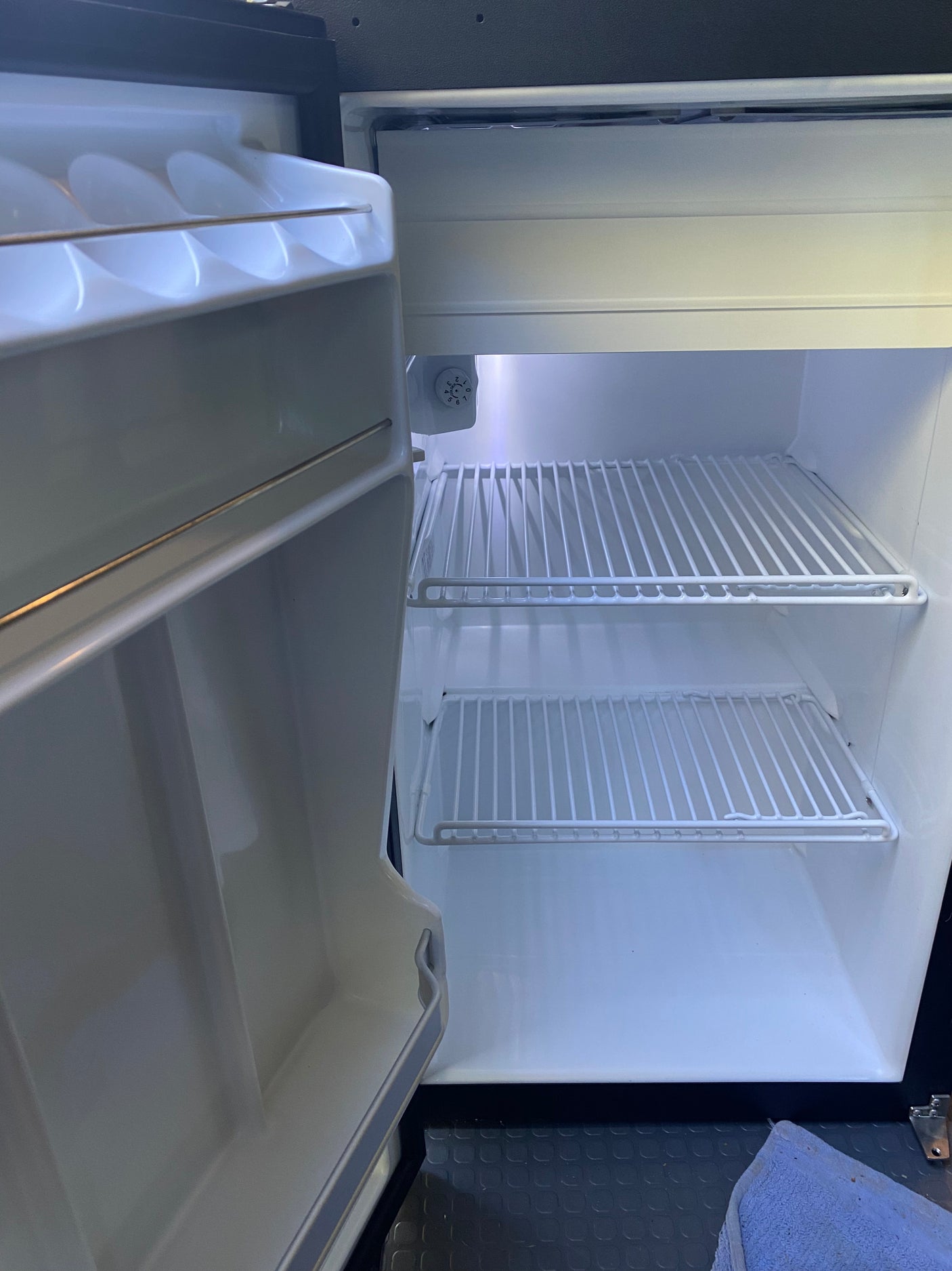 Empty, clean mini-fridge in an rv rental, with door open showing wire shelves and interior light. Ready for your trip!