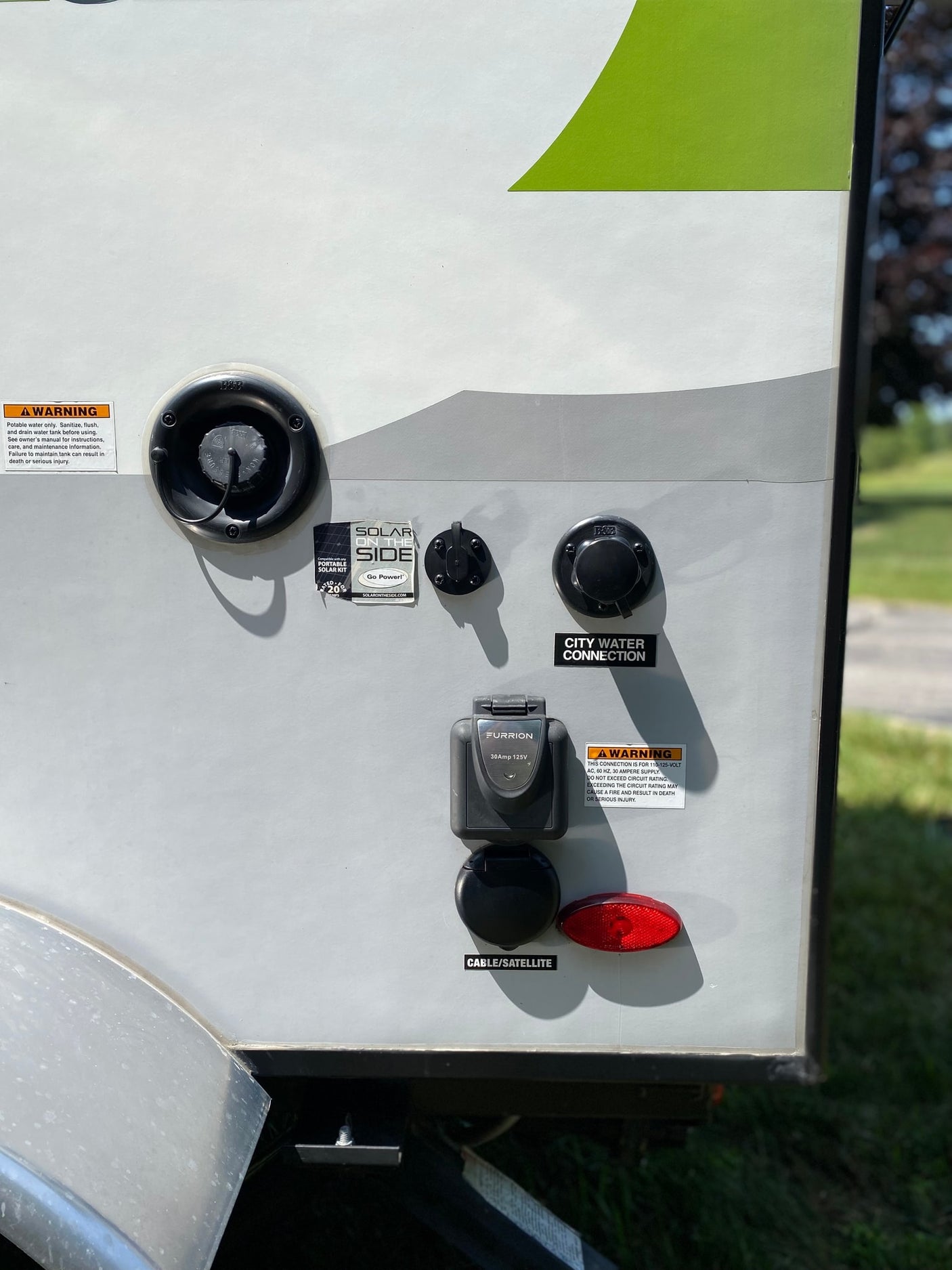 RV rental utility panel showing water, 30-amp shore power, solar, and cable hookups with safety warnings.